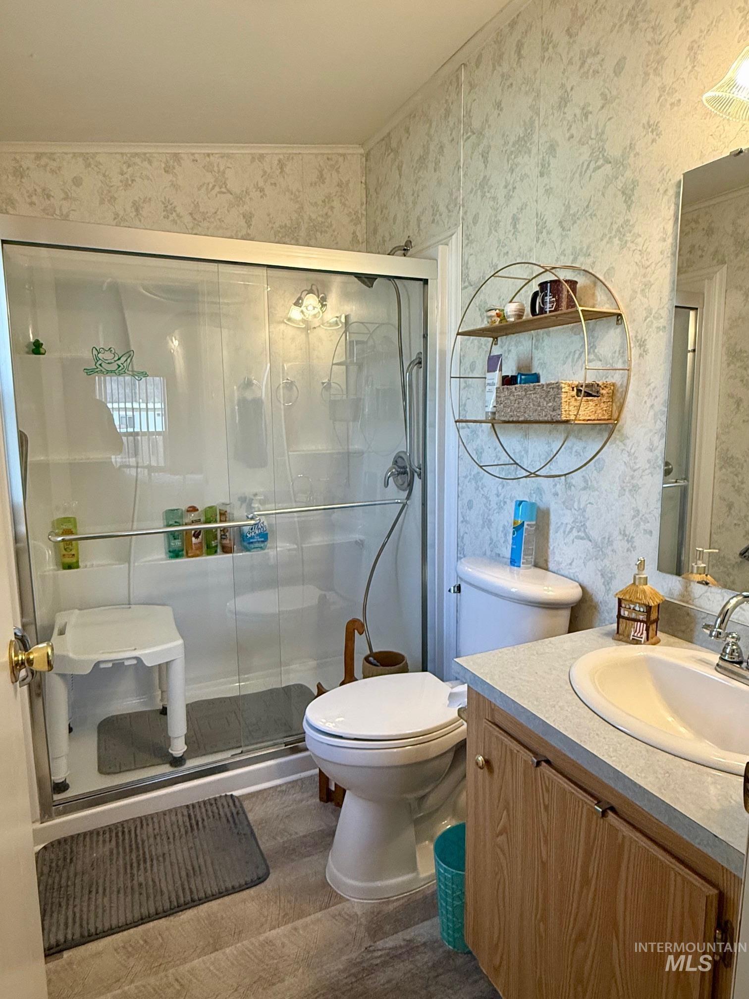 Full bath with vanity, wallpapered walls, a stall shower, and wood finished floors