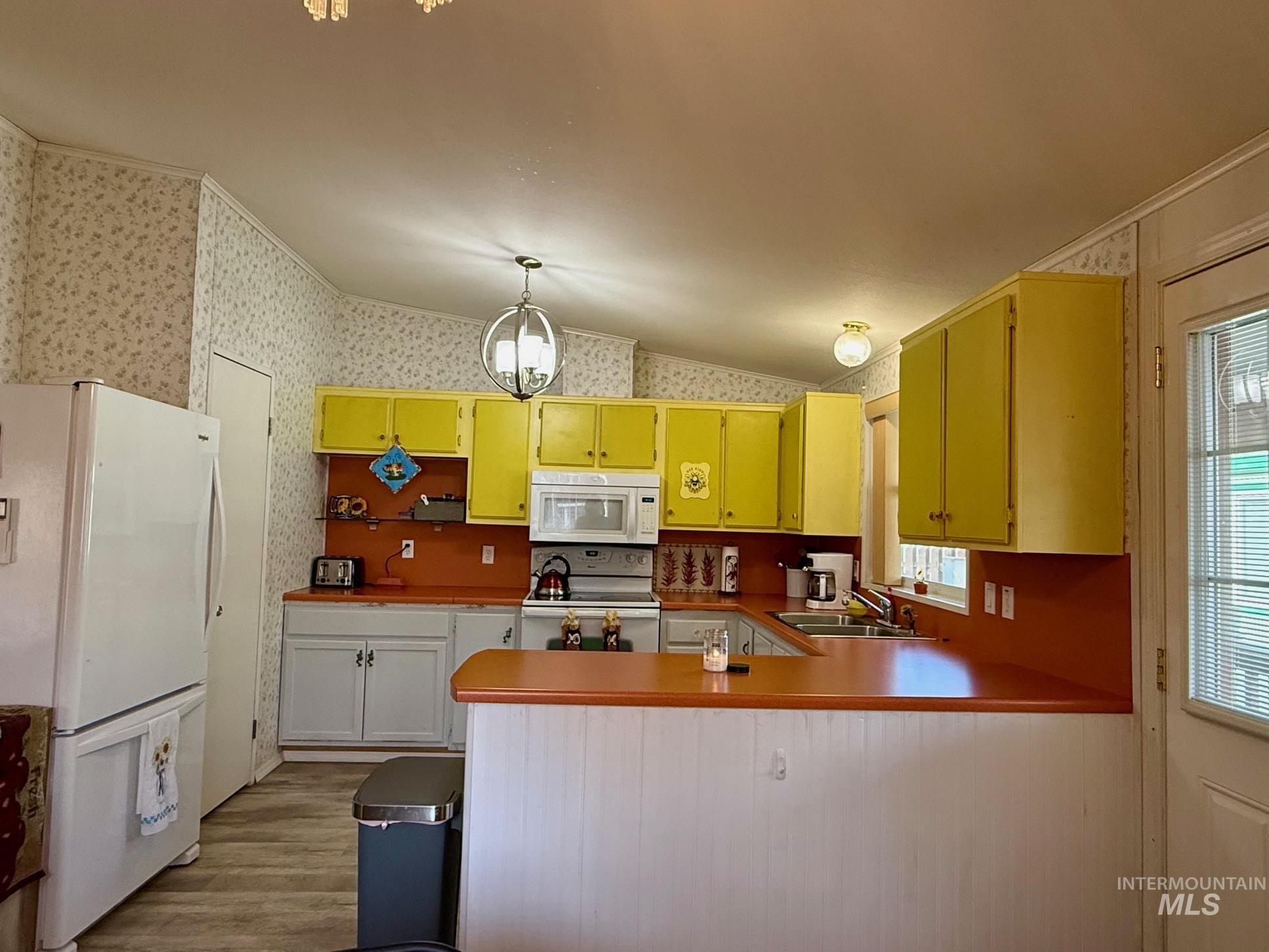 Kitchen with white appliances, lofted ceiling, a chandelier, a peninsula, and dark wood-style flooring