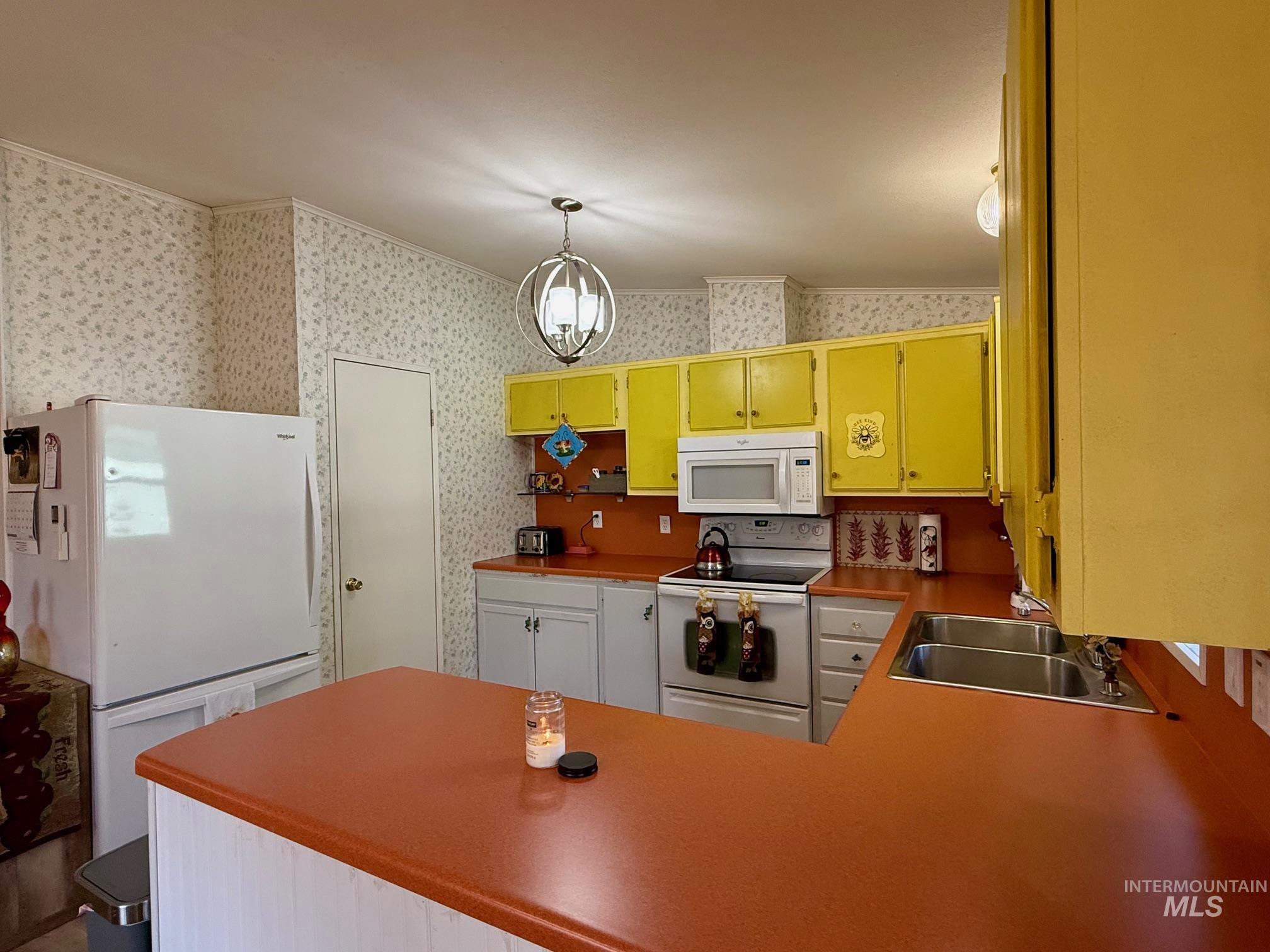 Kitchen featuring white appliances, hanging light fixtures, crown molding, wallpapered walls, and light countertops