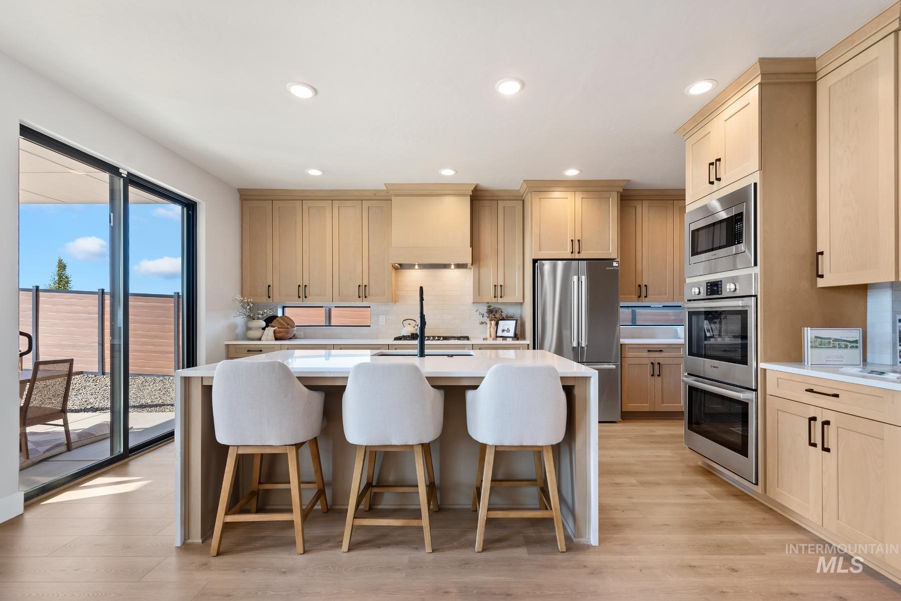 Kitchen featuring stainless steel appliances, a breakfast bar, light brown cabinetry, a center island with sink, and recessed lighting