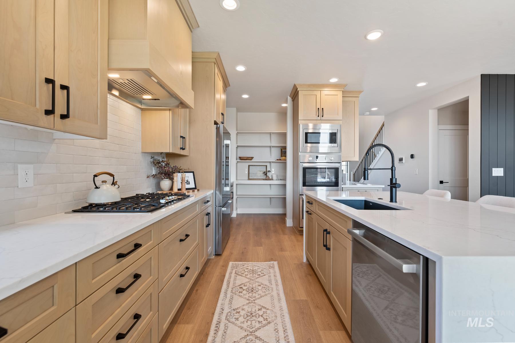 Kitchen with light stone countertops, stainless steel appliances, light wood-type flooring, a center island with sink, and custom exhaust hood