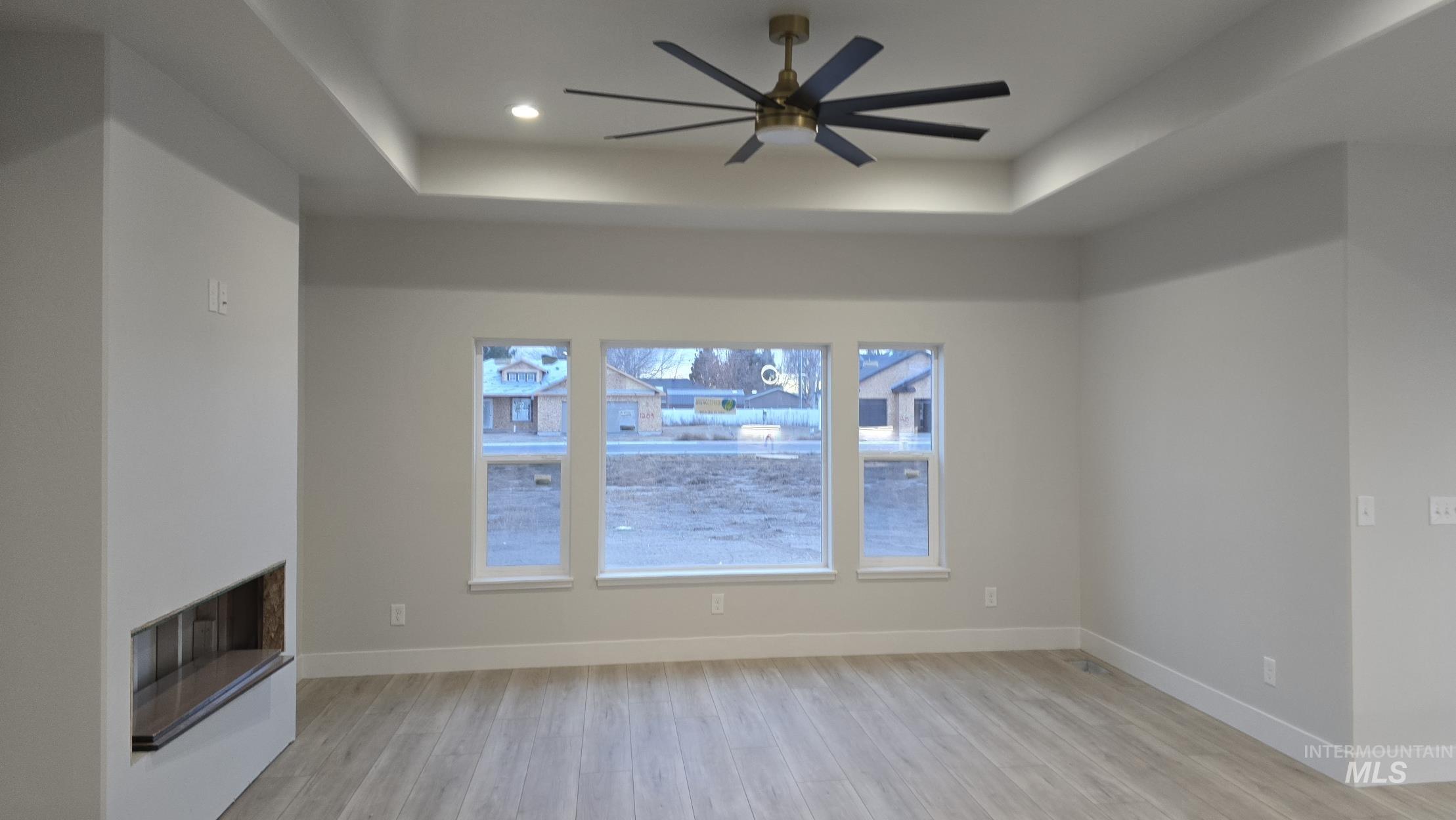 Unfurnished living room featuring a raised ceiling, light wood-style flooring, a fireplace with raised hearth, and a ceiling fan