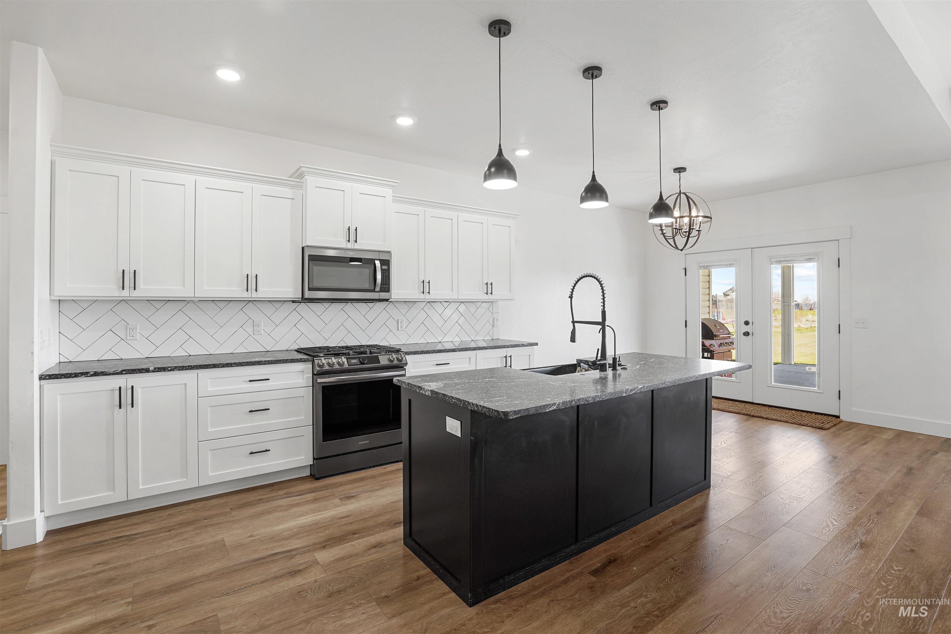 Kitchen with decorative backsplash, dark cabinets, appliances with stainless steel finishes, white cabinets, and a center island with sink