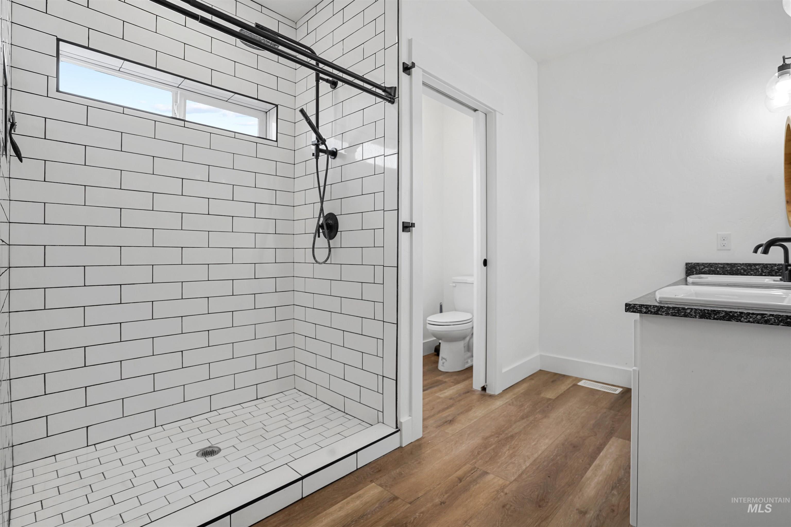 Full bath with double vanity, wood finished floors, and a shower stall