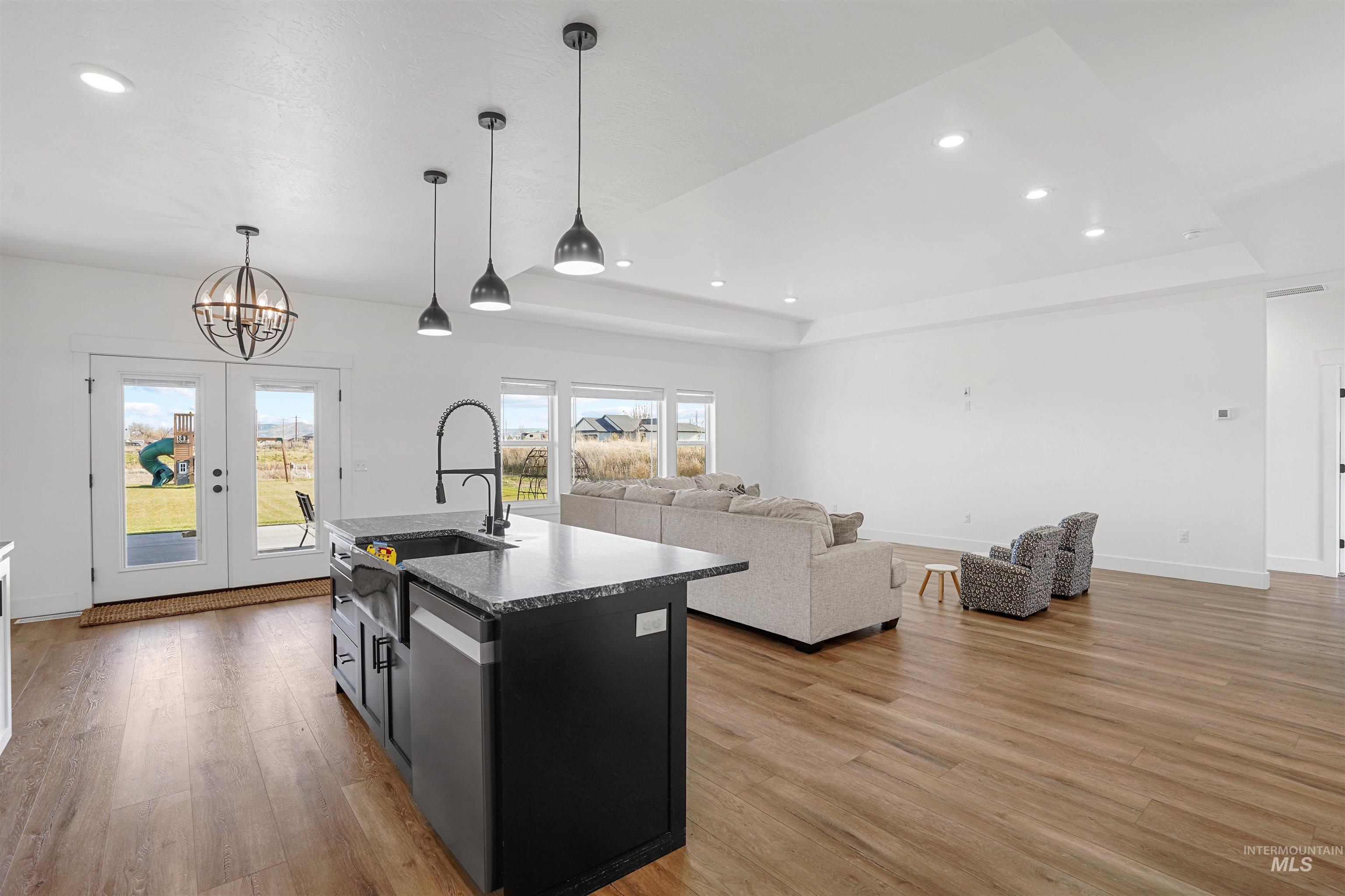 Kitchen with a raised ceiling, hanging light fixtures, a center island with sink, recessed lighting, and open floor plan
