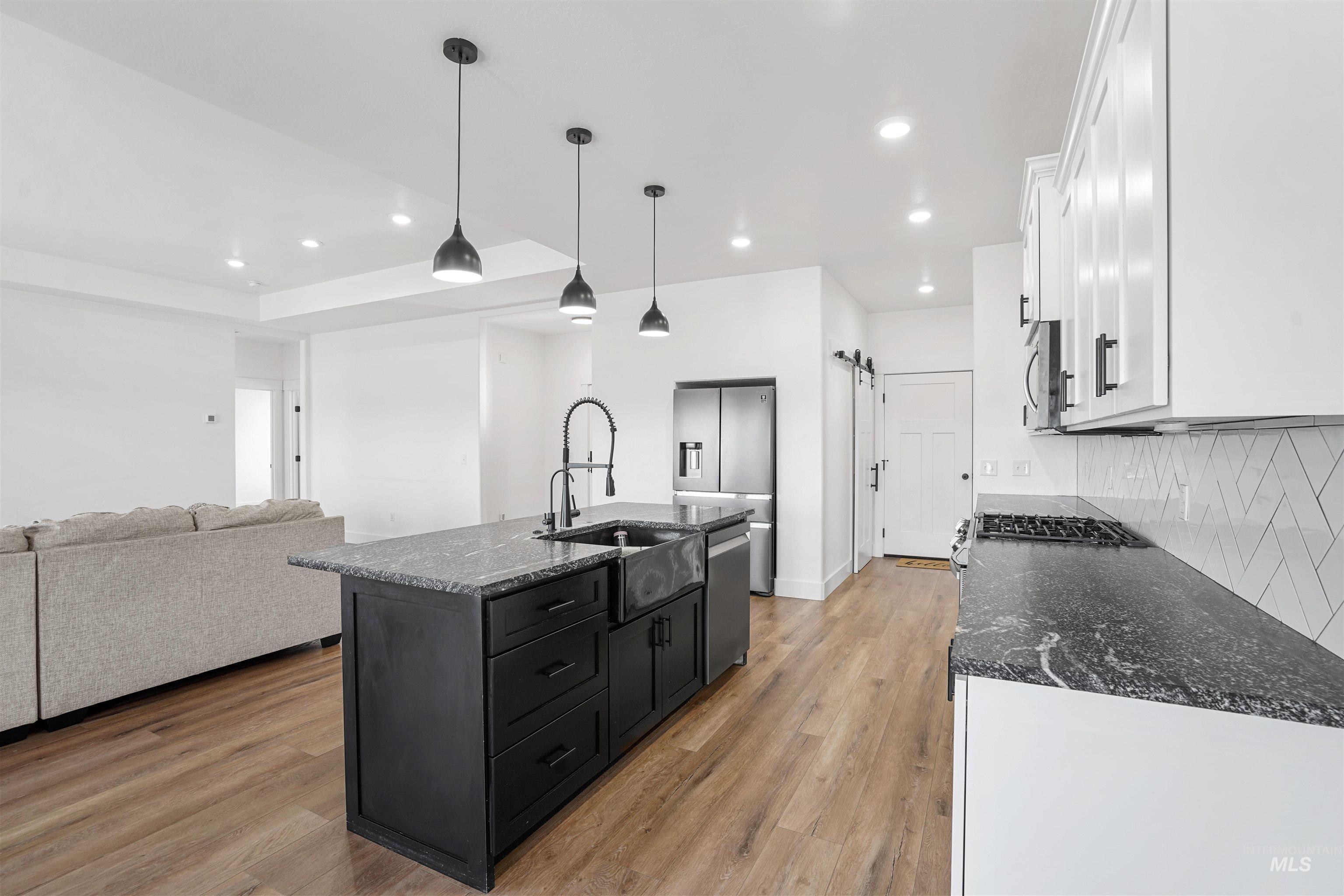 Kitchen featuring dark stone countertops, an island with sink, white cabinetry, hanging light fixtures, and open floor plan