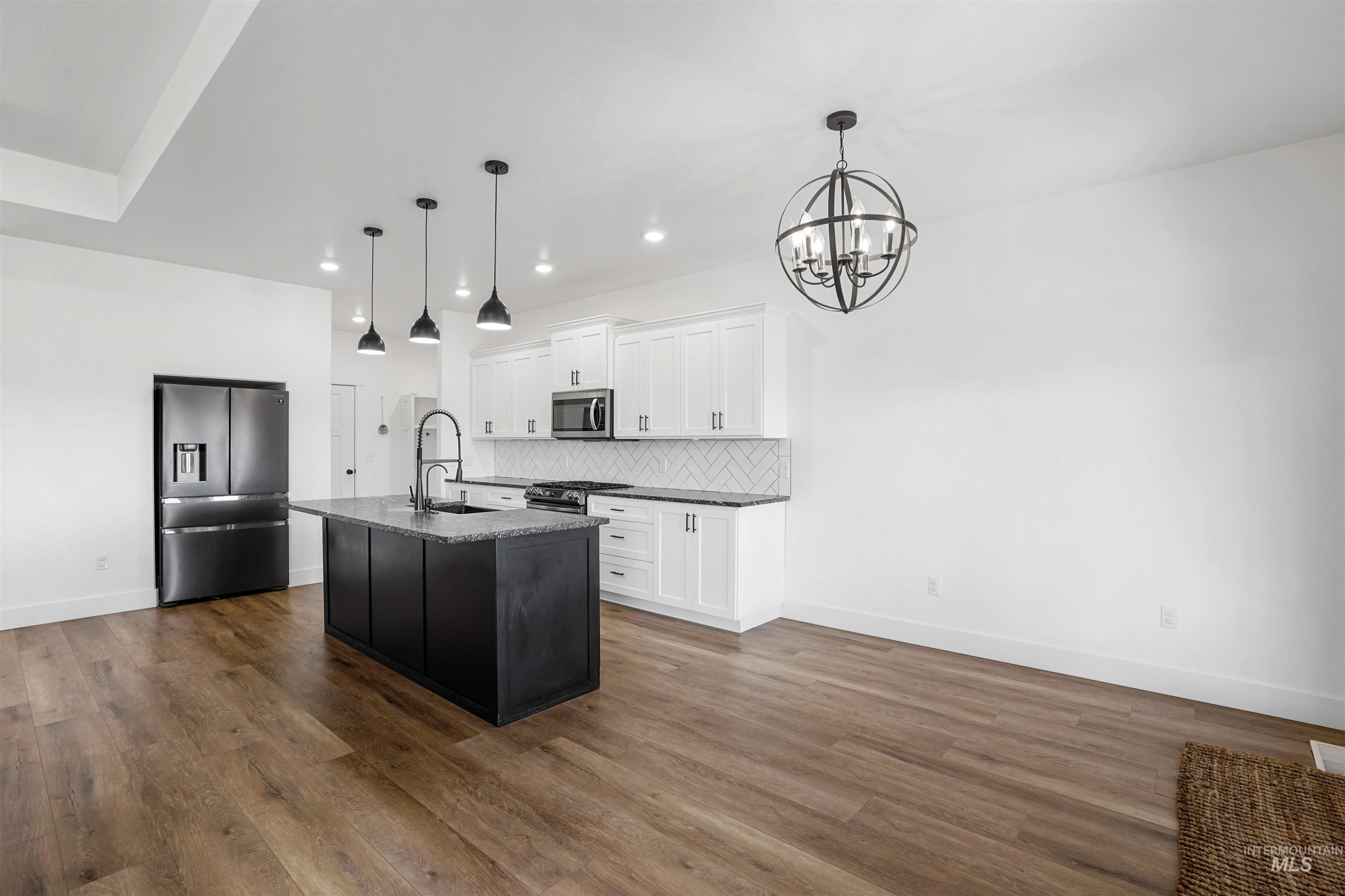 Kitchen with tasteful backsplash, white cabinetry, appliances with stainless steel finishes, an island with sink, and decorative light fixtures