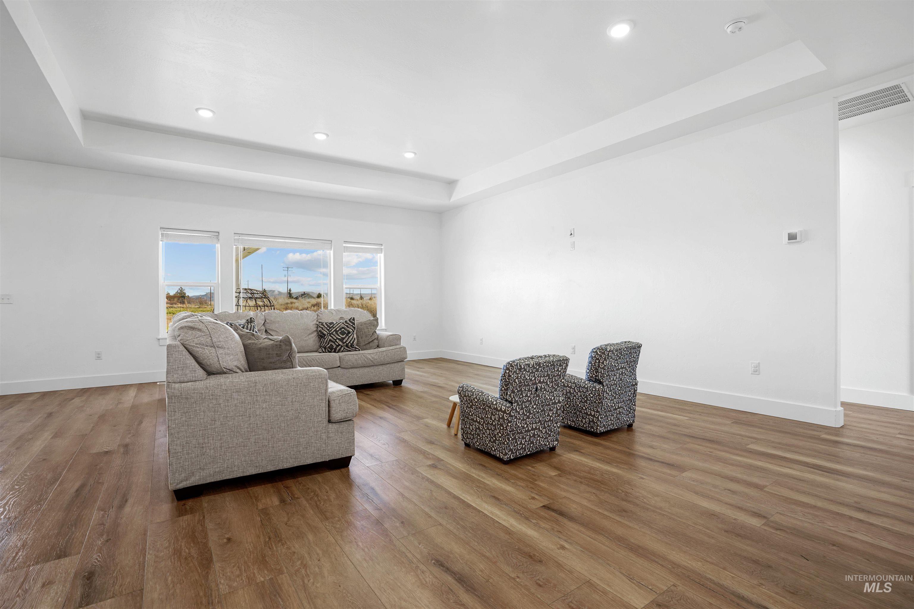 Living area featuring a raised ceiling, recessed lighting, and wood finished floors