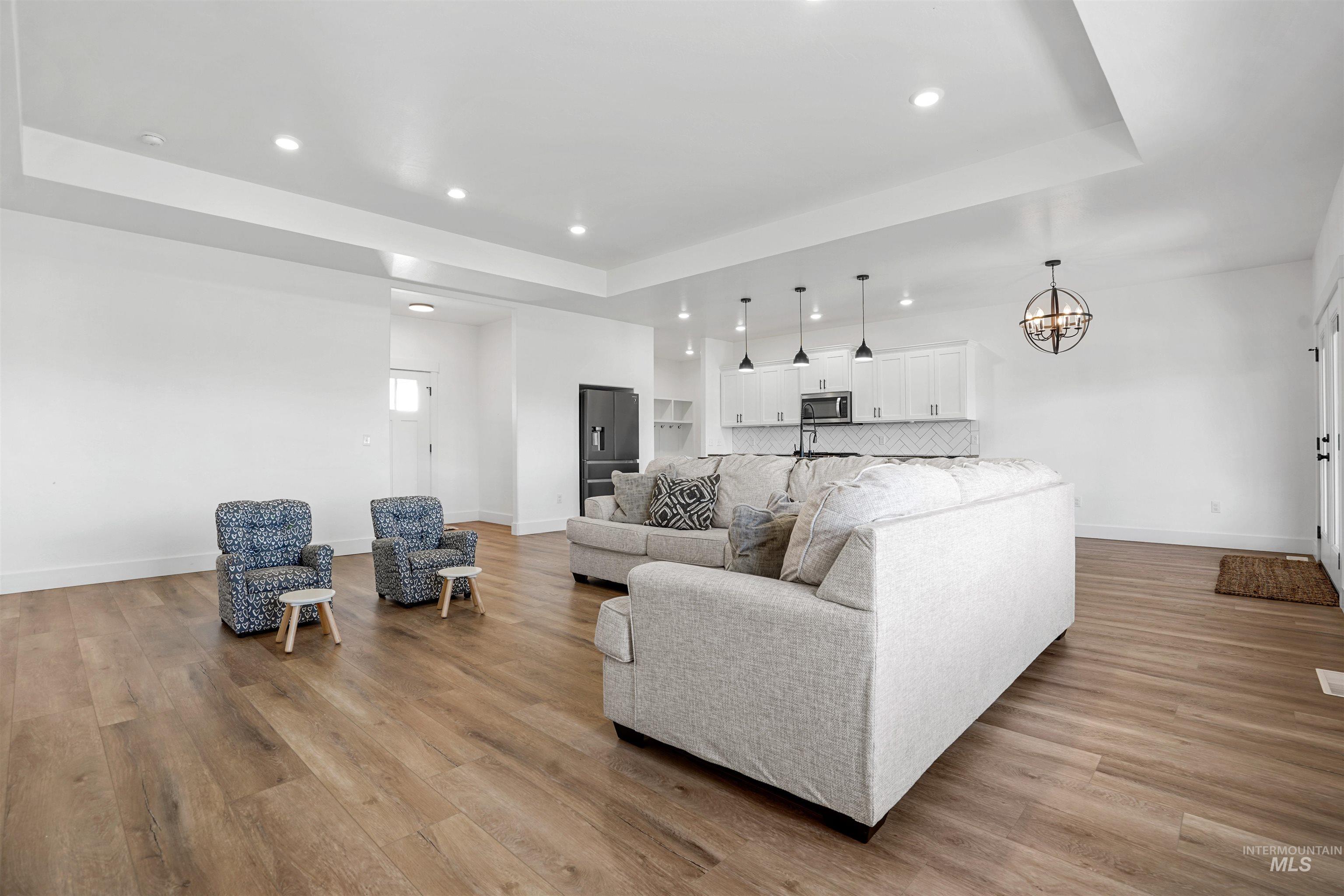 Living room with a tray ceiling, recessed lighting, light wood finished floors, and a chandelier