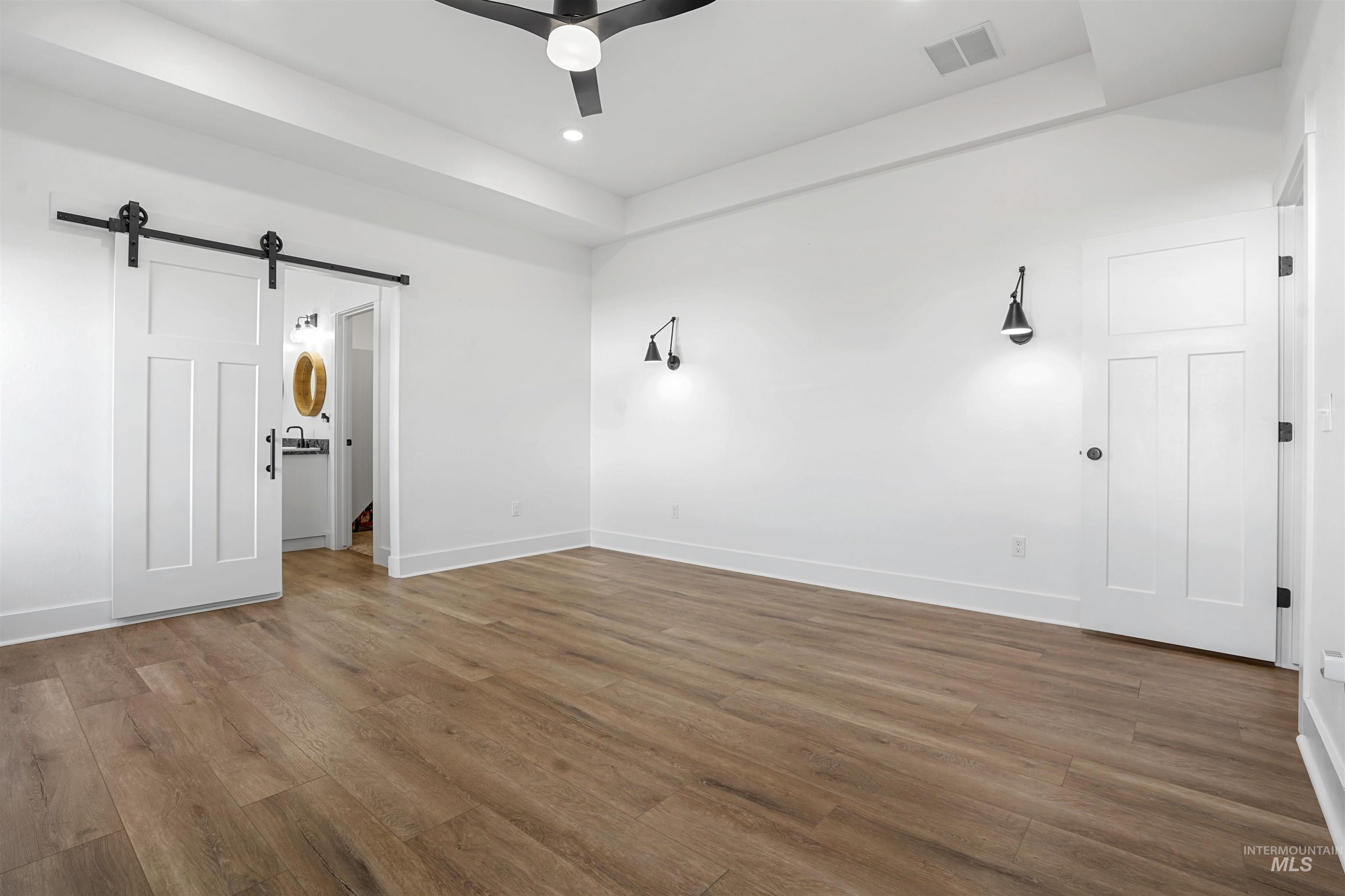 Unfurnished bedroom with a barn door, wood finished floors, recessed lighting, ceiling fan, and ensuite bathroom