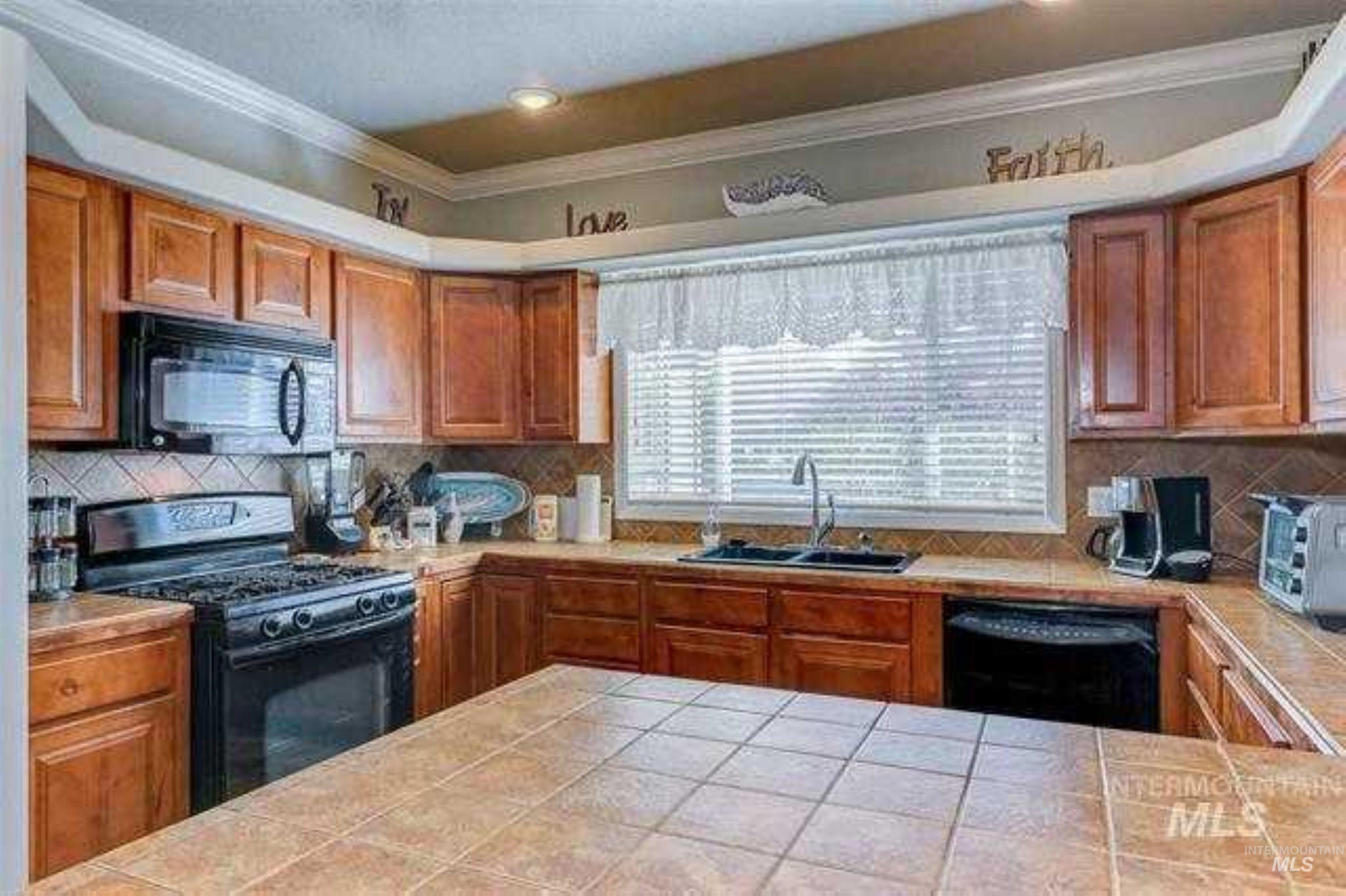 Kitchen with black appliances, brown cabinets, backsplash, and crown molding