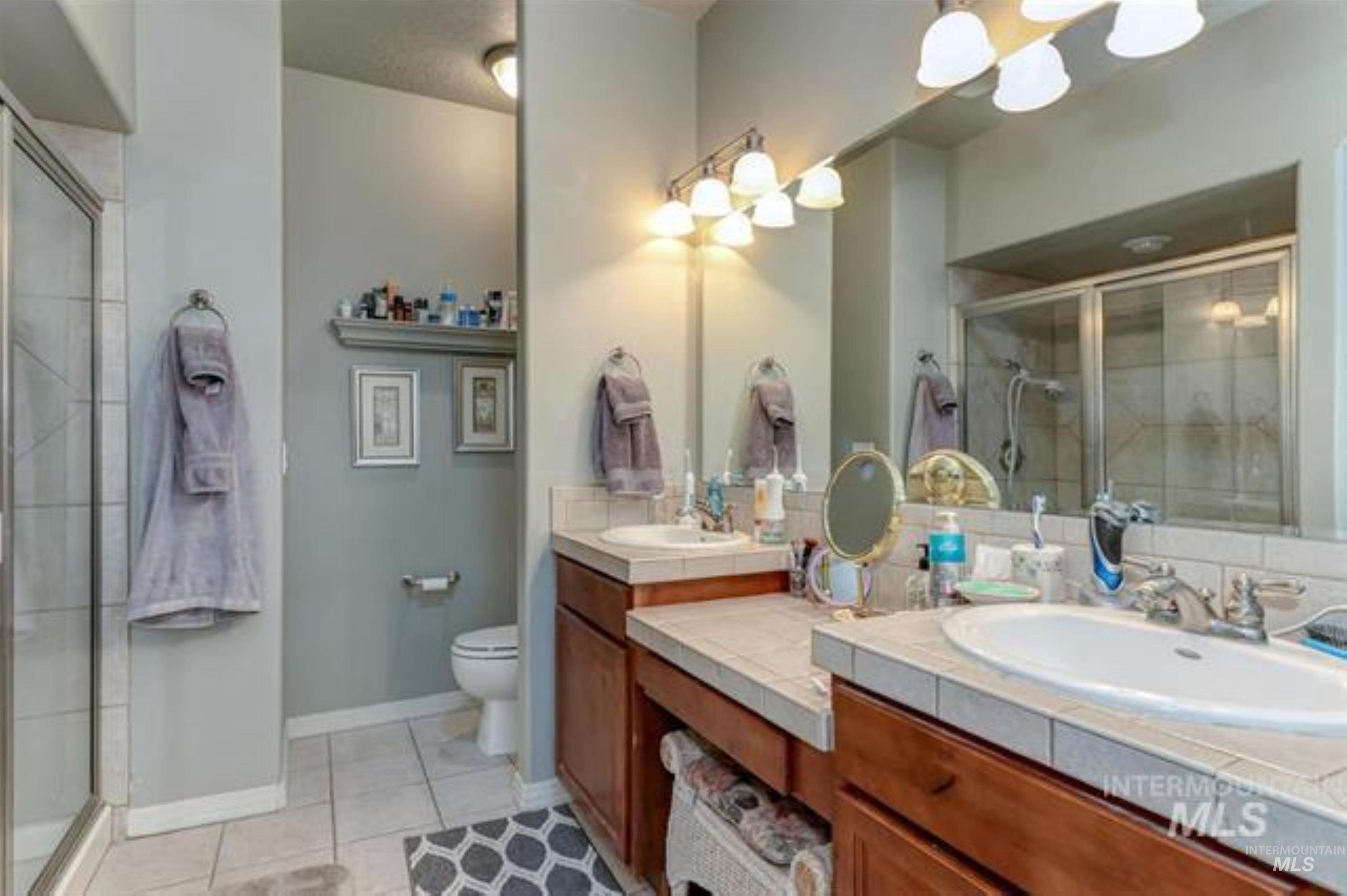 Full bath with a shower stall, double vanity, and light tile patterned floors