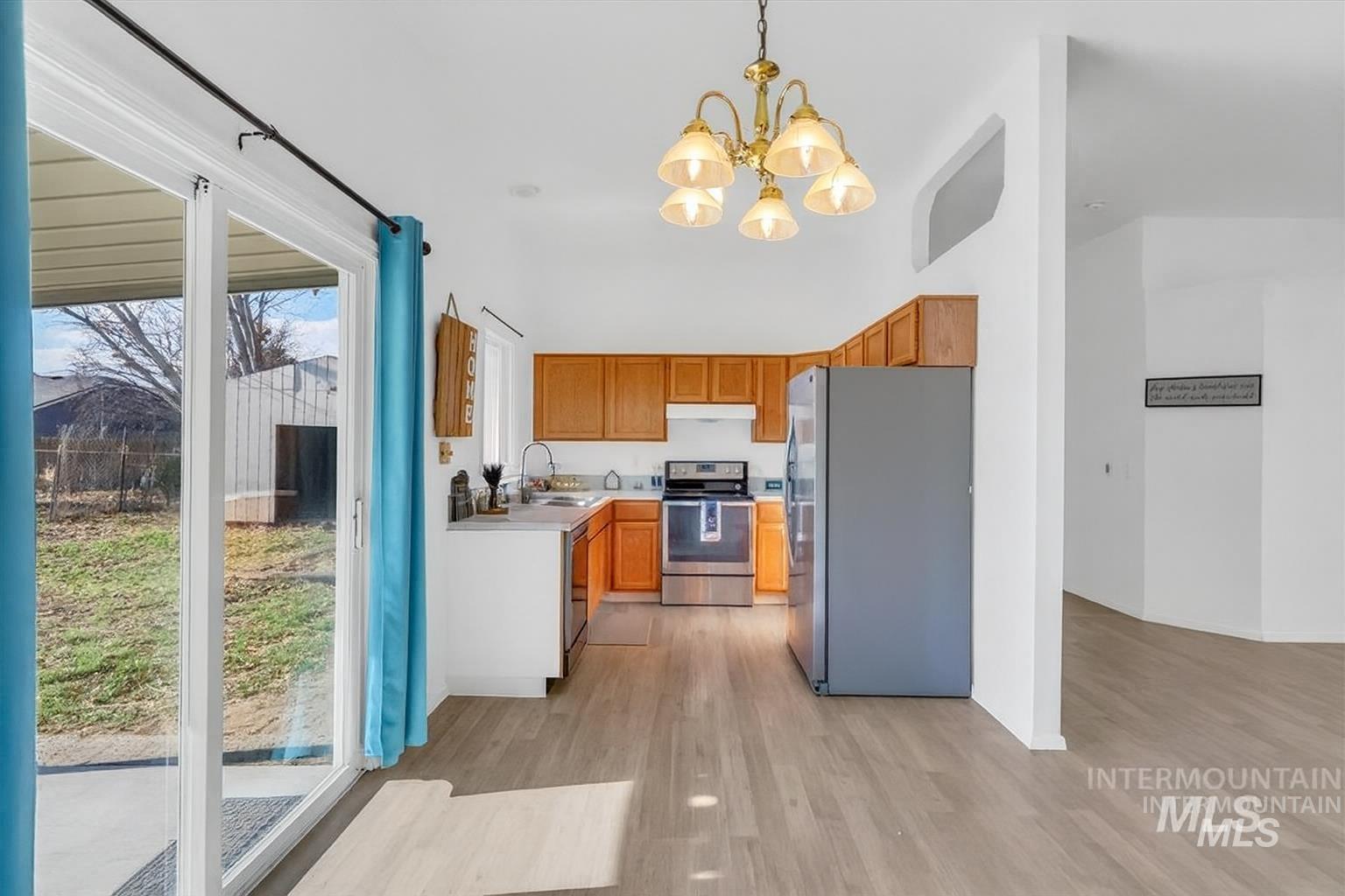 Kitchen with light countertops, appliances with stainless steel finishes, pendant lighting, brown cabinets, and light wood-type flooring