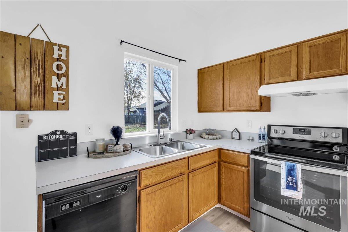 Kitchen with electric range, light countertops, dishwasher, under cabinet range hood, and brown cabinetry