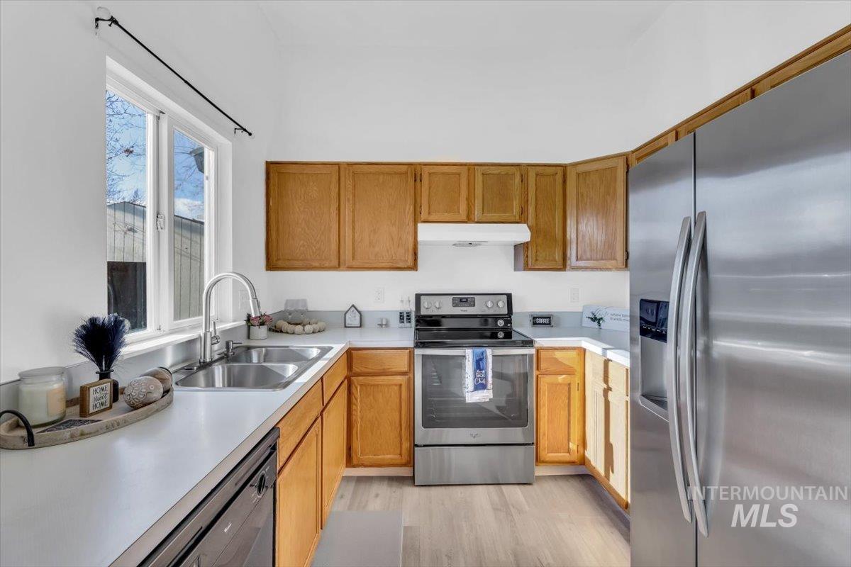 Kitchen featuring appliances with stainless steel finishes, light countertops, brown cabinets, under cabinet range hood, and light wood-style floors