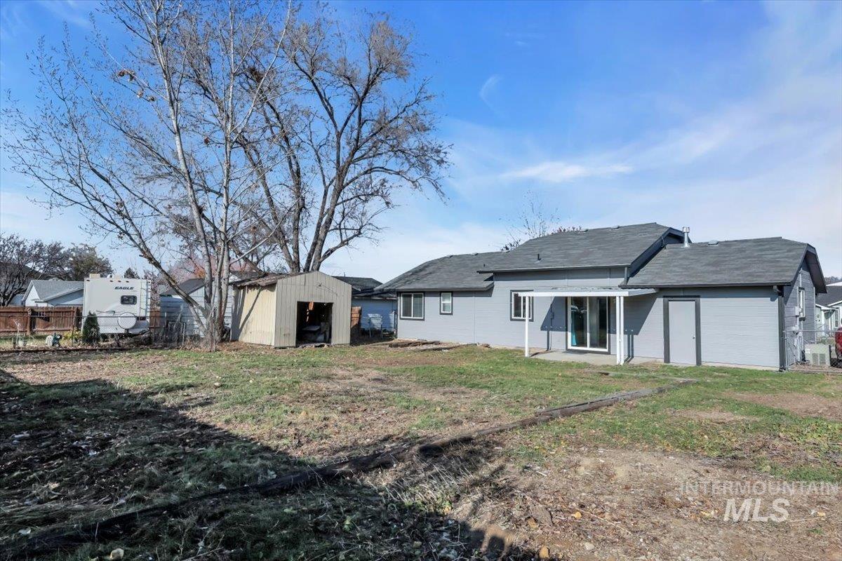 Back of property featuring a storage unit, a patio area, and a shingled roof