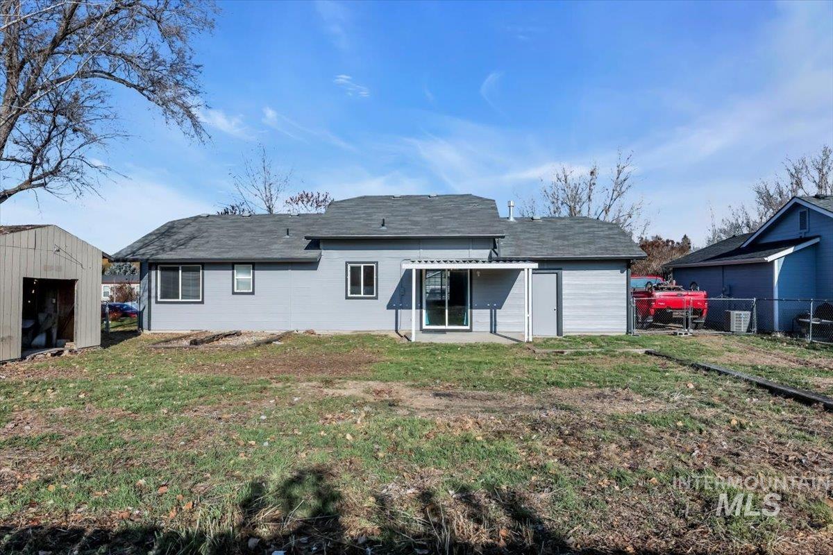 Rear view of house featuring a patio, a storage unit, and a shingled roof