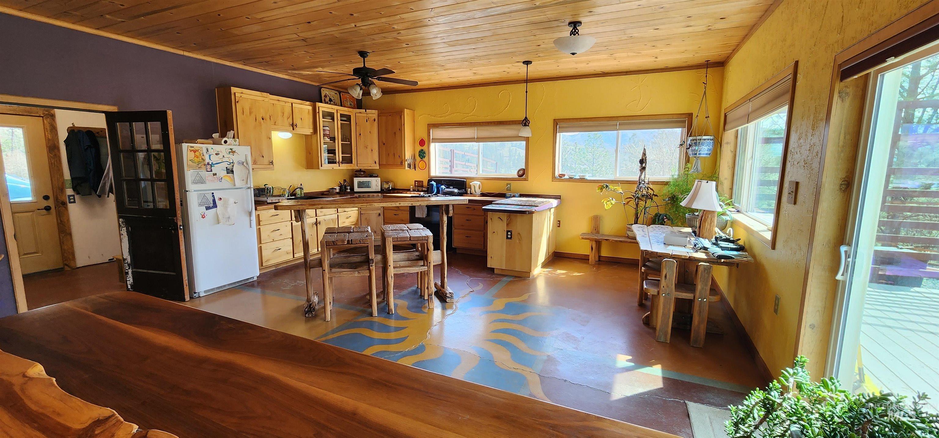 Kitchen with wooden ceiling, freestanding refrigerator, hanging light fixtures, glass insert cabinets, and a ceiling fan
