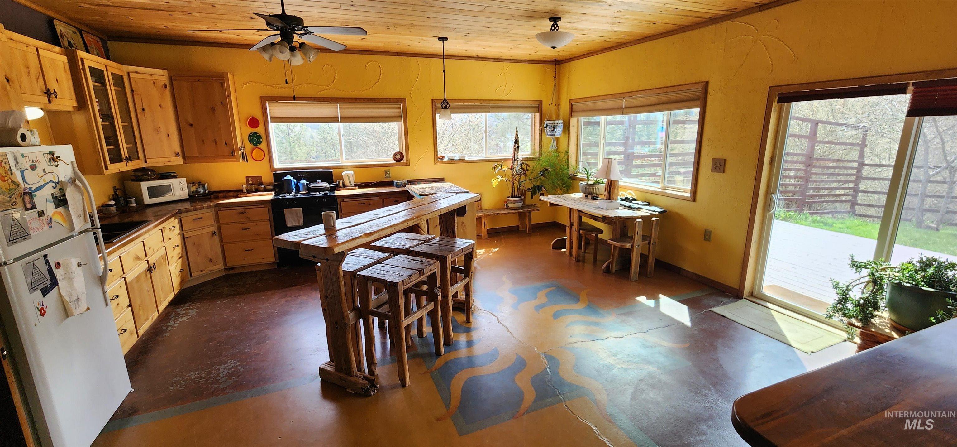 Kitchen with wooden ceiling, dark countertops, white appliances, glass insert cabinets, and concrete floors