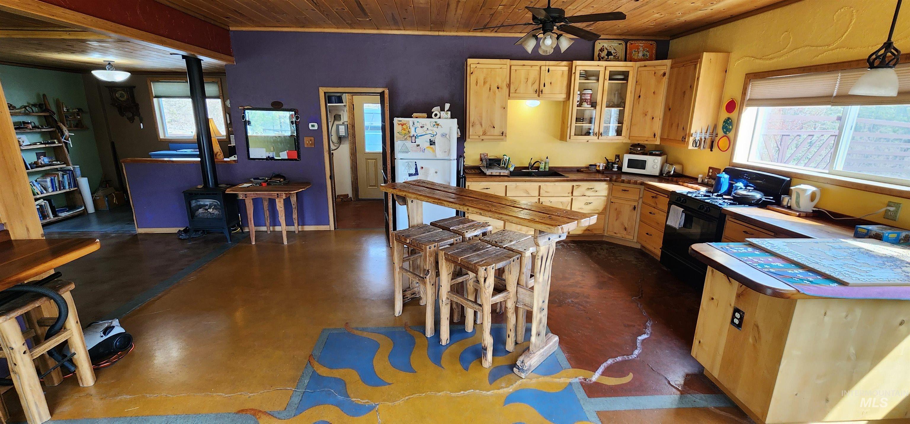 Kitchen featuring wooden ceiling, light brown cabinets, a wood stove, white appliances, and a ceiling fan