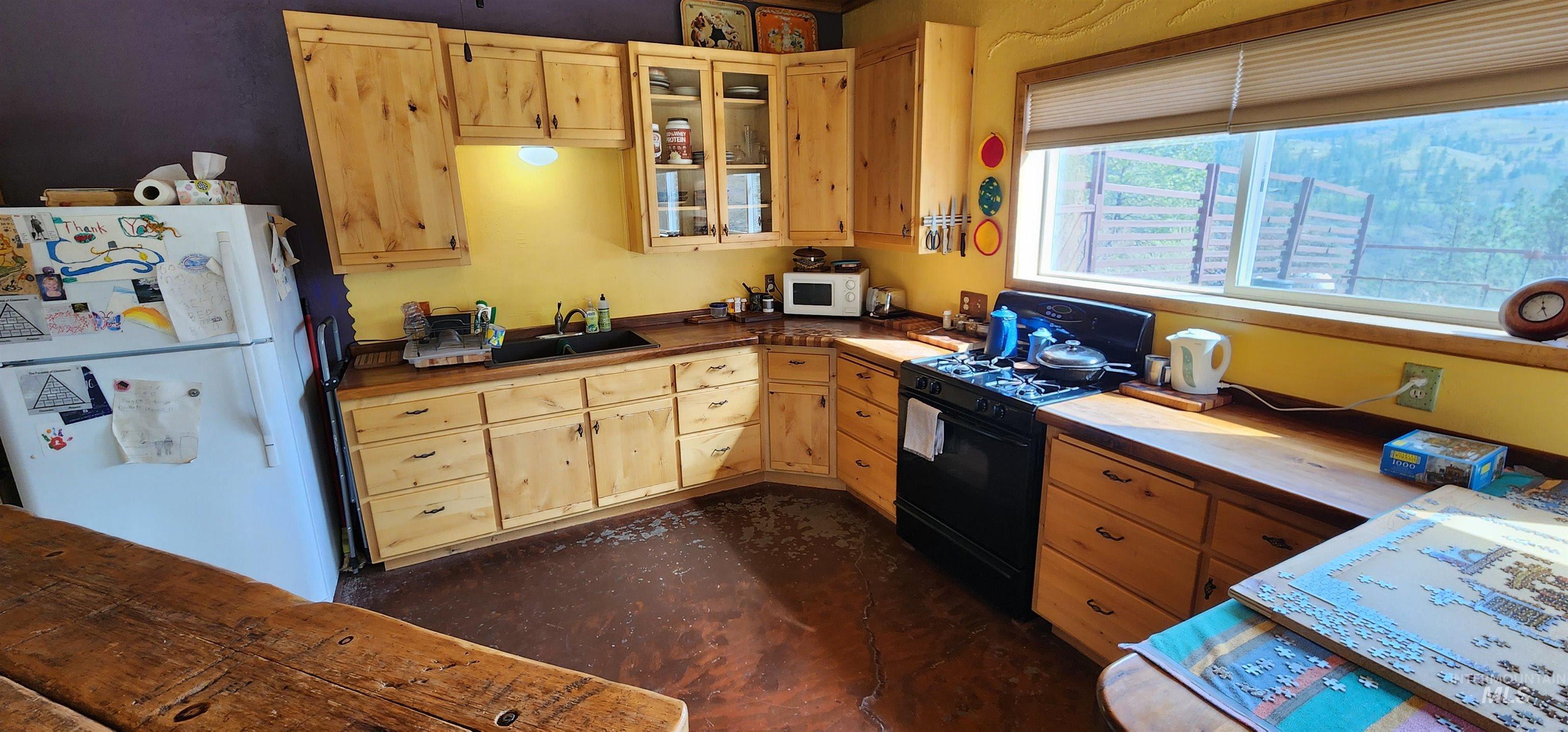 Kitchen featuring white appliances, glass insert cabinets, light brown cabinetry, and wooden counters