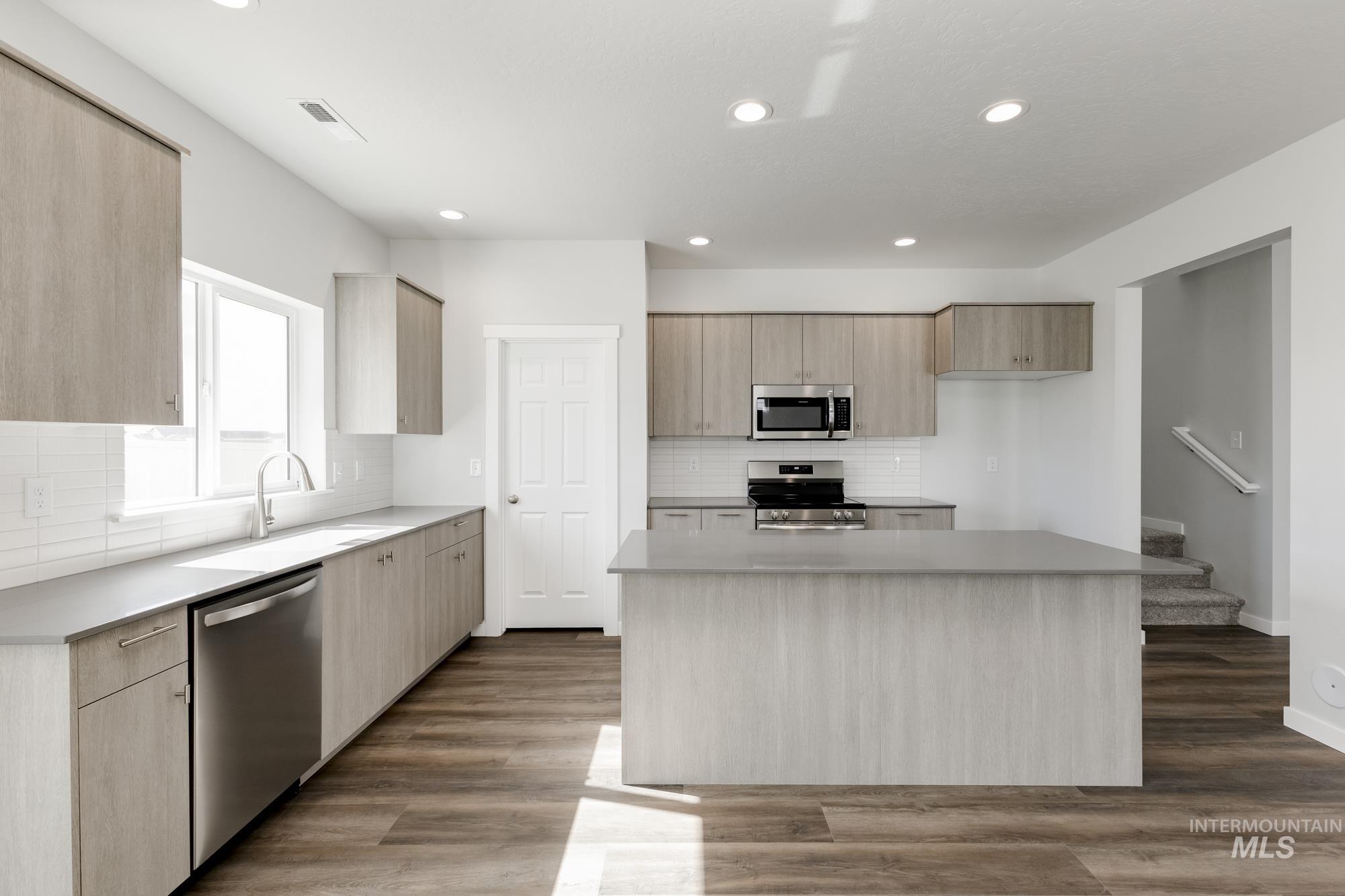 Kitchen featuring light brown cabinetry, appliances with stainless steel finishes, modern cabinets, backsplash, and a kitchen island