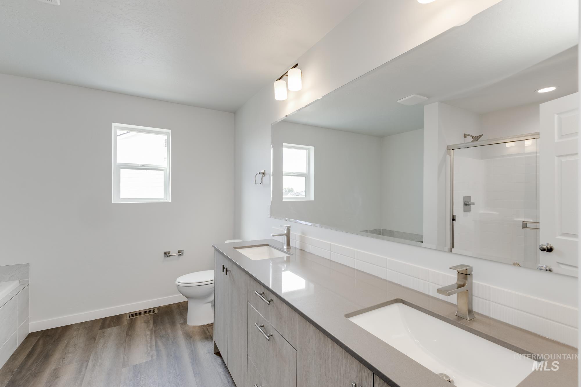 Bathroom with double vanity, a shower stall, dark wood-type flooring, and a tub