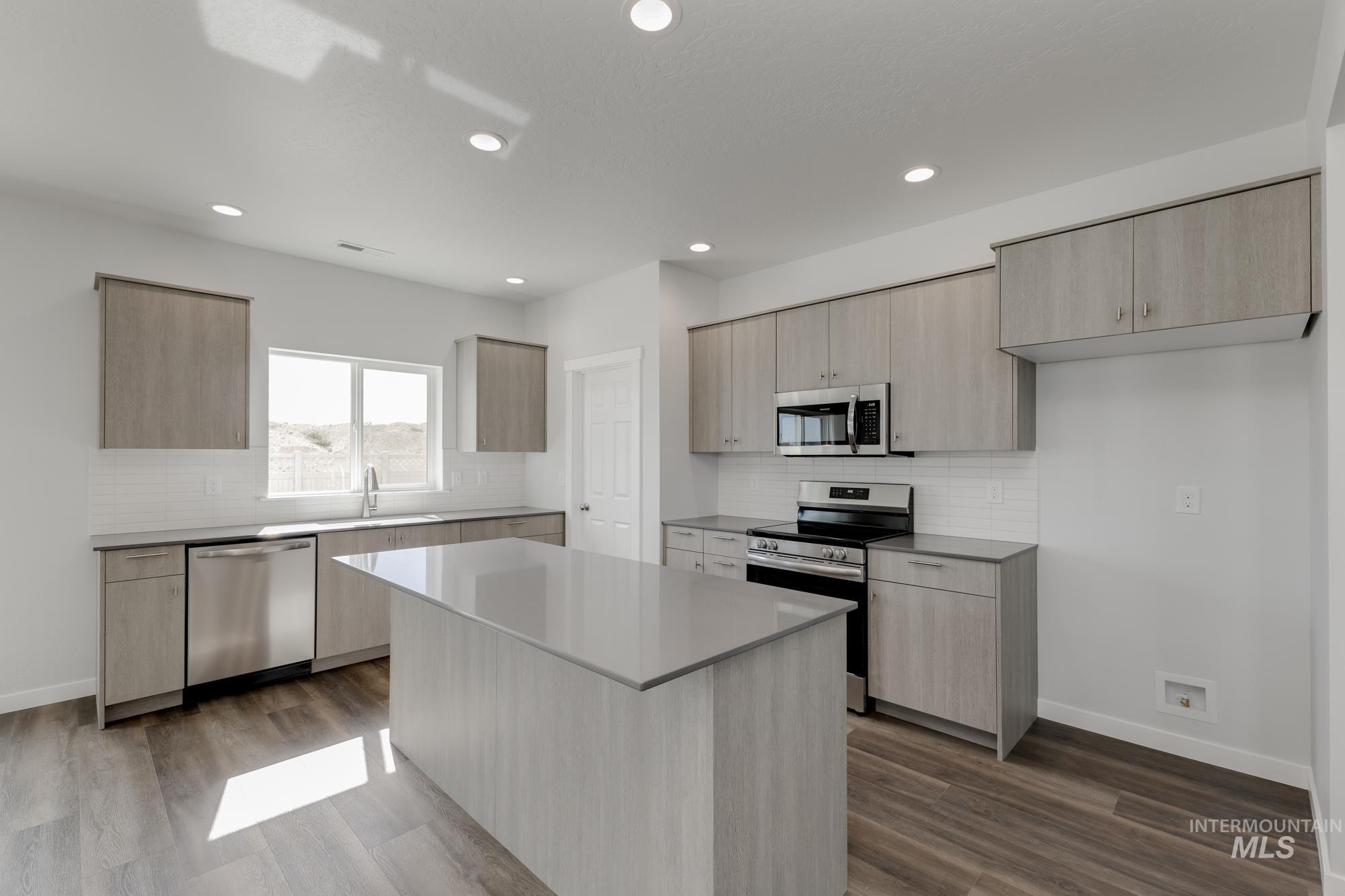 Kitchen featuring light brown cabinetry, stainless steel appliances, backsplash, modern cabinets, and dark wood finished floors