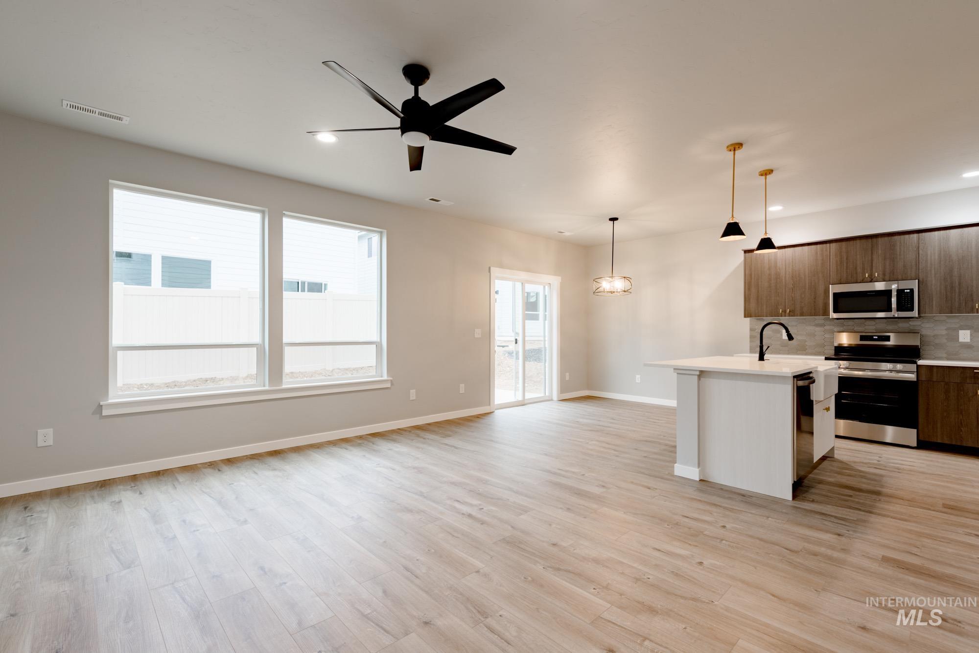 Kitchen featuring appliances with stainless steel finishes, open floor plan, a kitchen island with sink, hanging light fixtures, and plenty of natural light