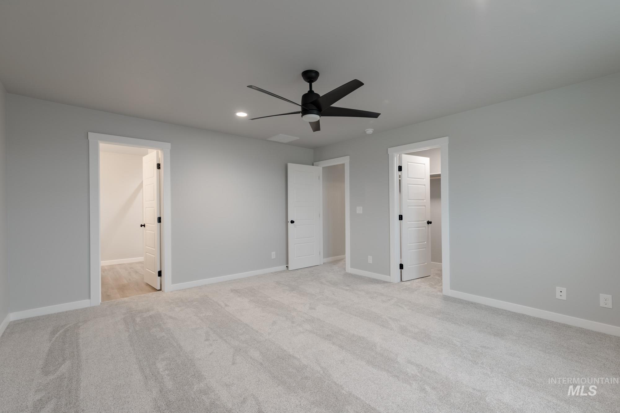 Unfurnished bedroom featuring light colored carpet, a spacious closet, a ceiling fan, recessed lighting, and ensuite bathroom