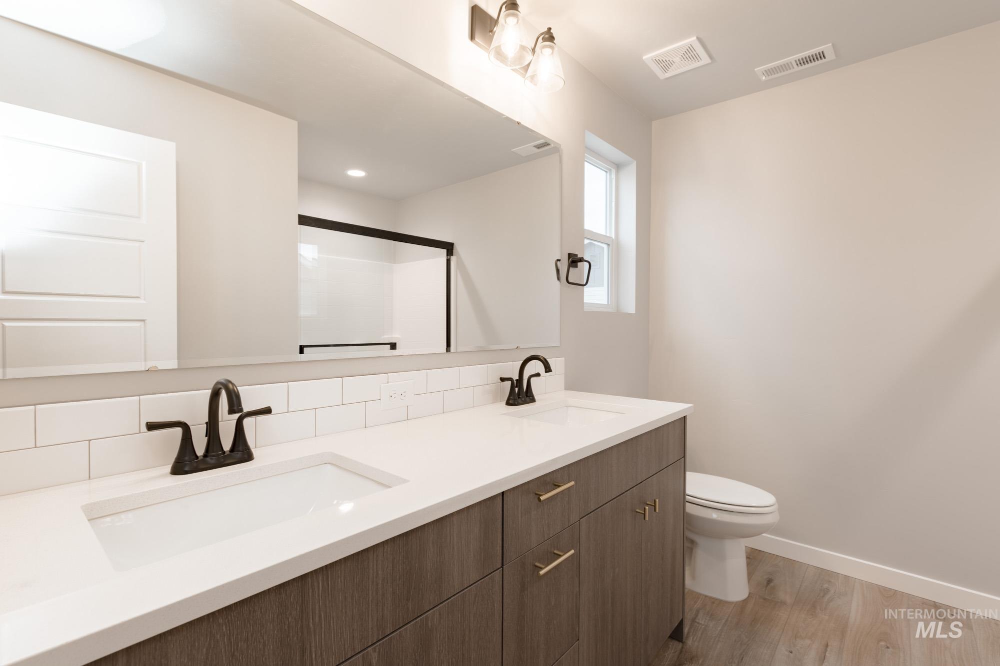 Full bath with light wood-type flooring, double vanity, a stall shower, and backsplash