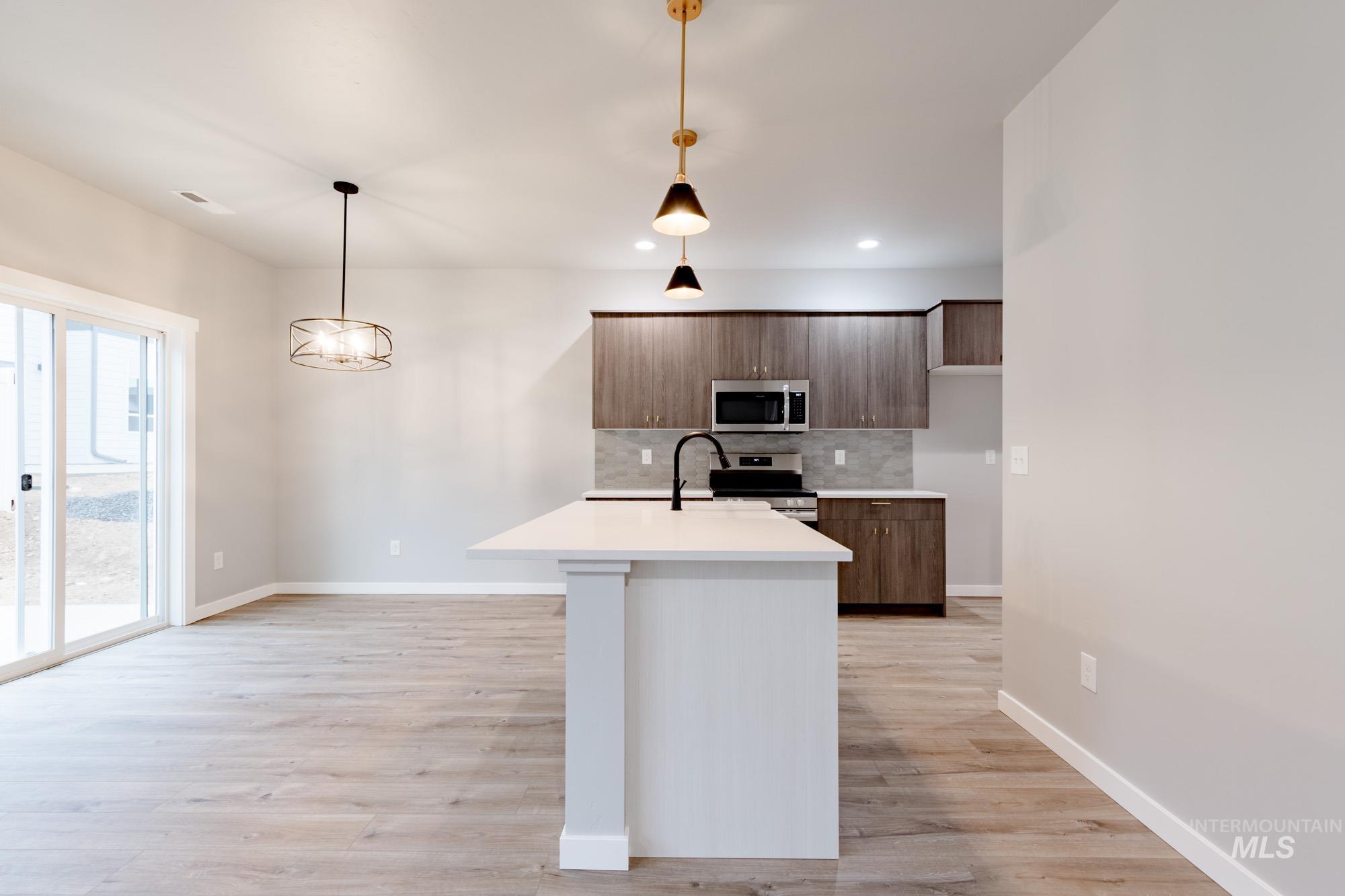 Kitchen with tasteful backsplash, appliances with stainless steel finishes, hanging light fixtures, a kitchen island with sink, and light wood-style floors