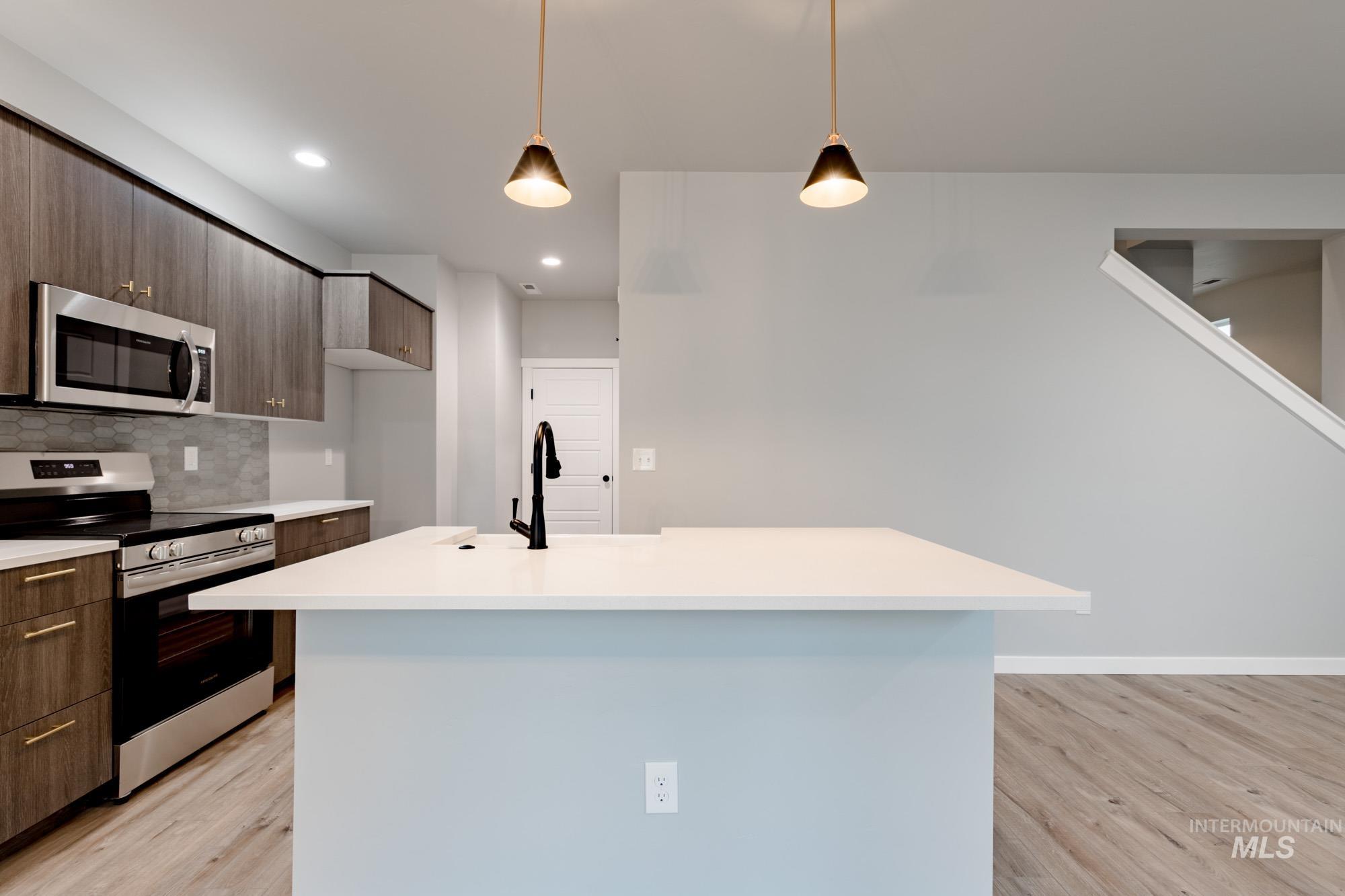 Kitchen featuring modern cabinets, appliances with stainless steel finishes, light wood-type flooring, backsplash, and decorative light fixtures