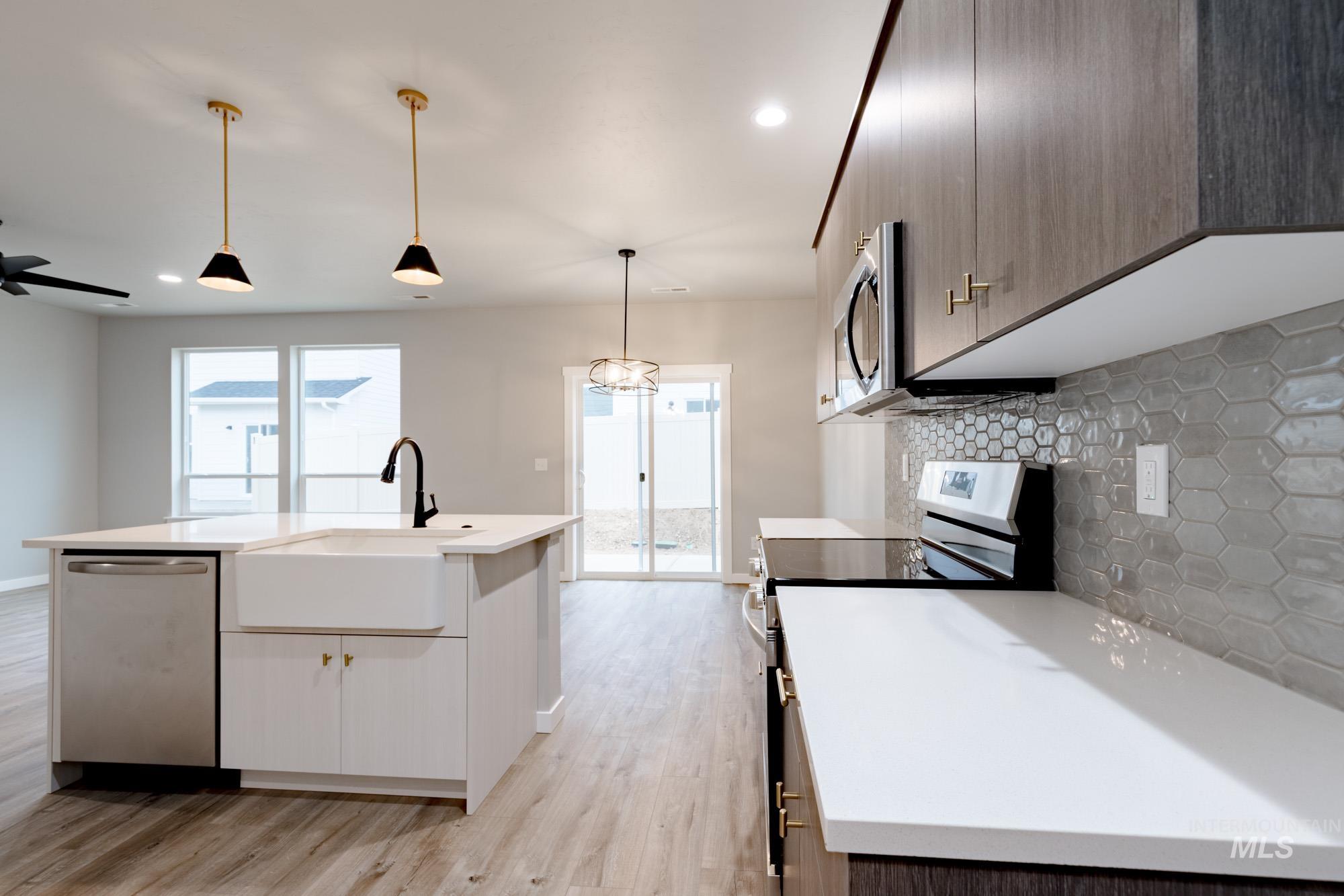 Kitchen with stainless steel appliances, decorative backsplash, decorative light fixtures, light wood-style floors, and a center island with sink
