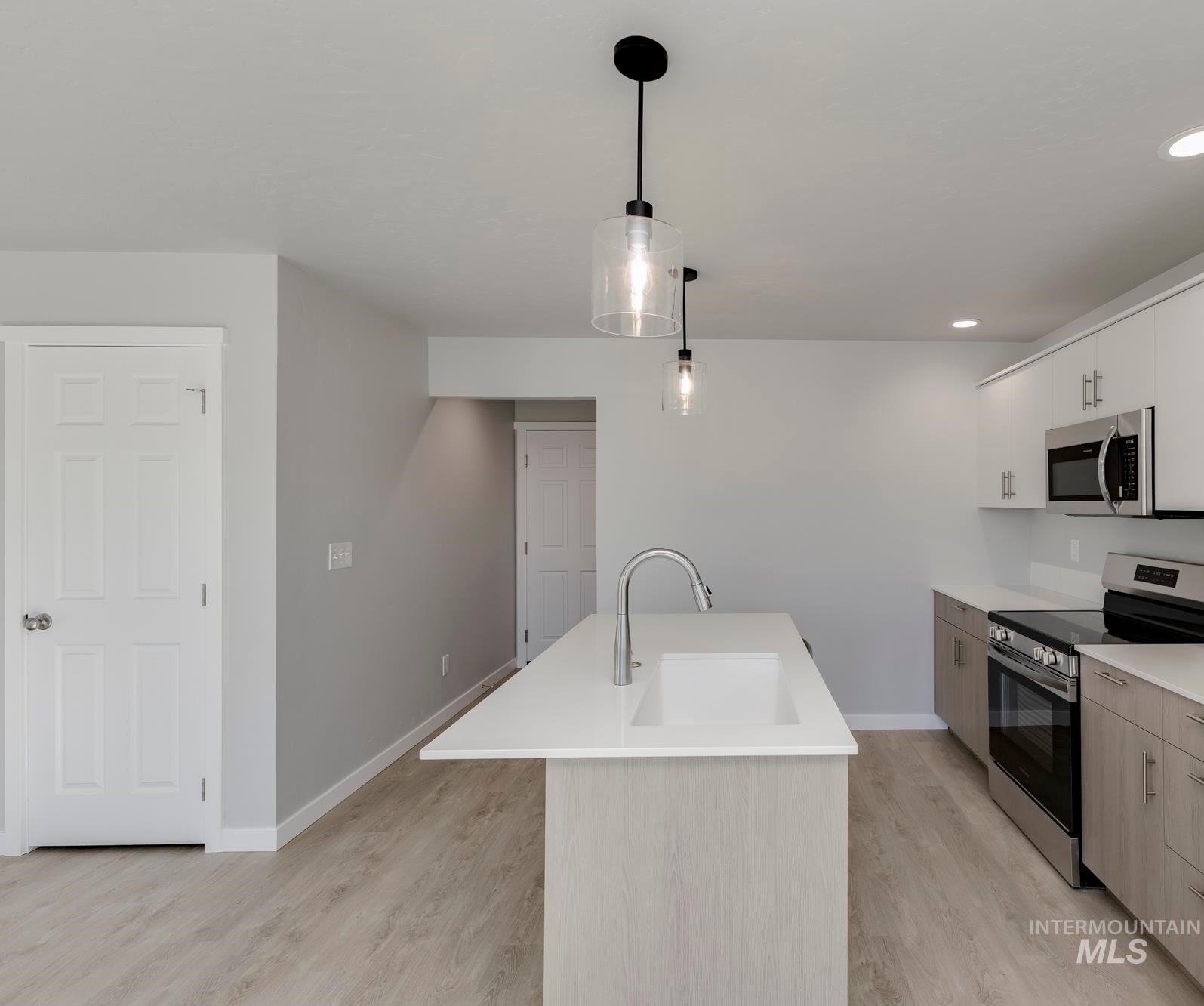 Kitchen with stainless steel appliances, light wood-style floors, hanging light fixtures, recessed lighting, and white cabinets
