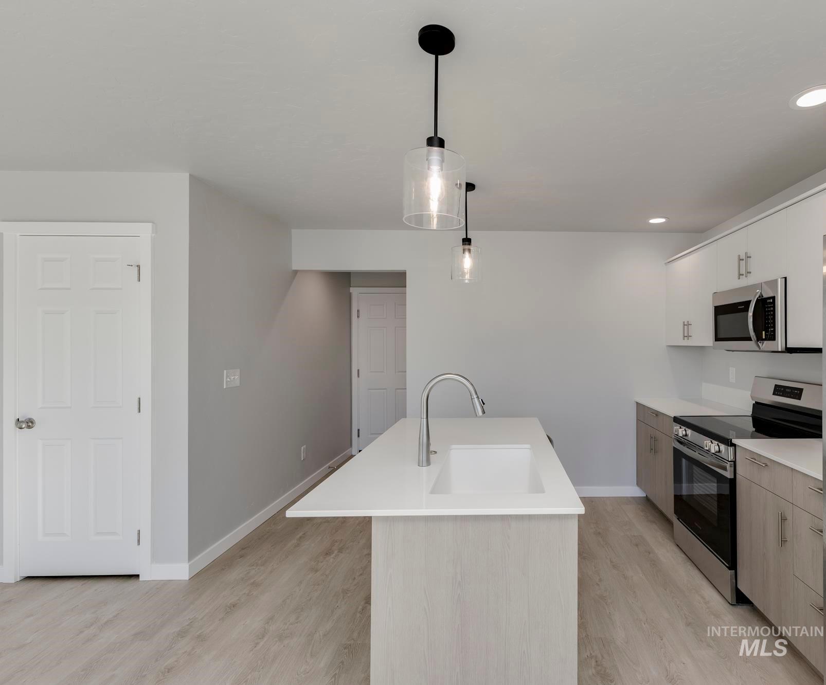 Kitchen with stainless steel appliances, light wood-style floors, hanging light fixtures, recessed lighting, and white cabinets