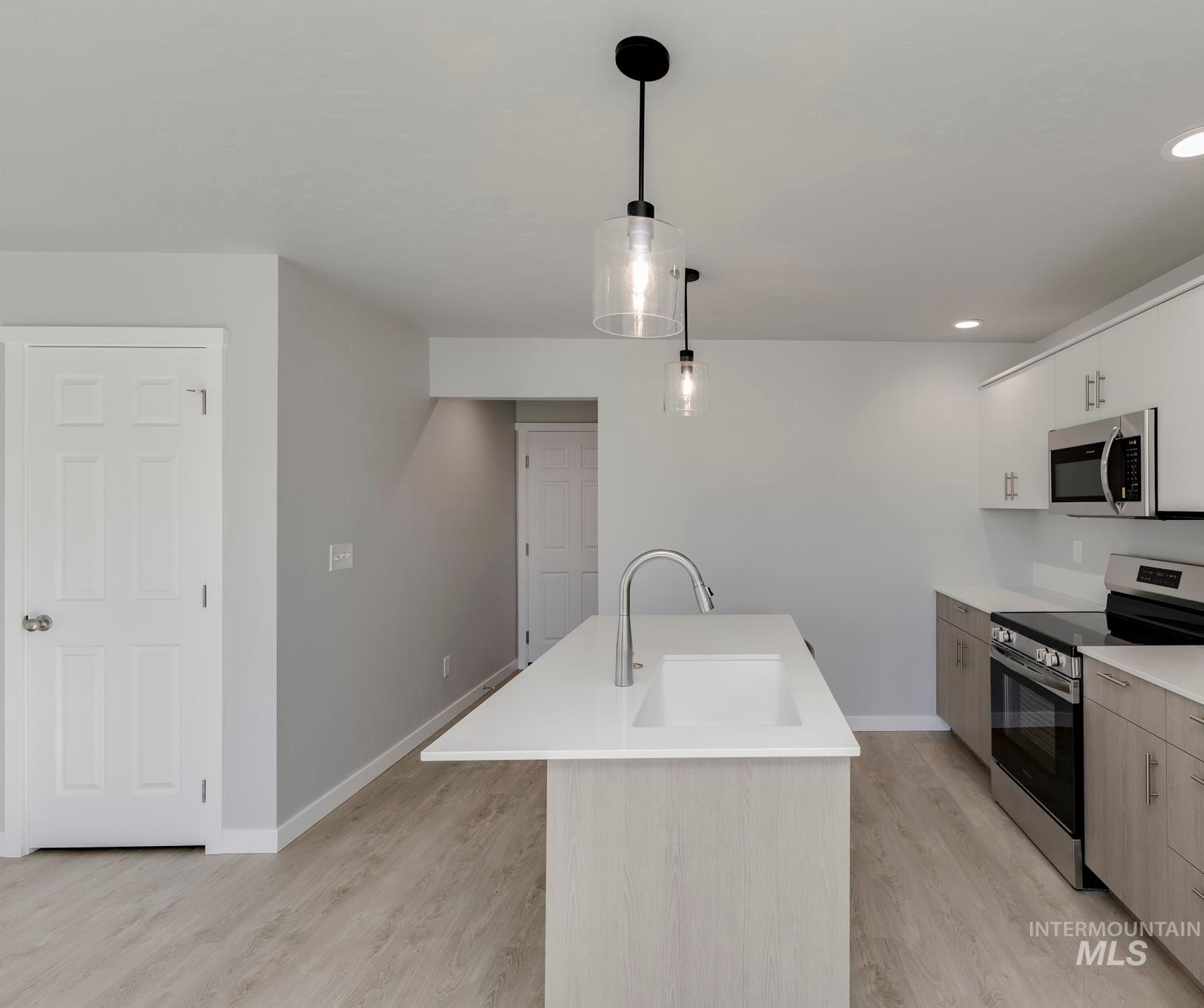Kitchen with stainless steel appliances, light wood-style floors, hanging light fixtures, recessed lighting, and white cabinets