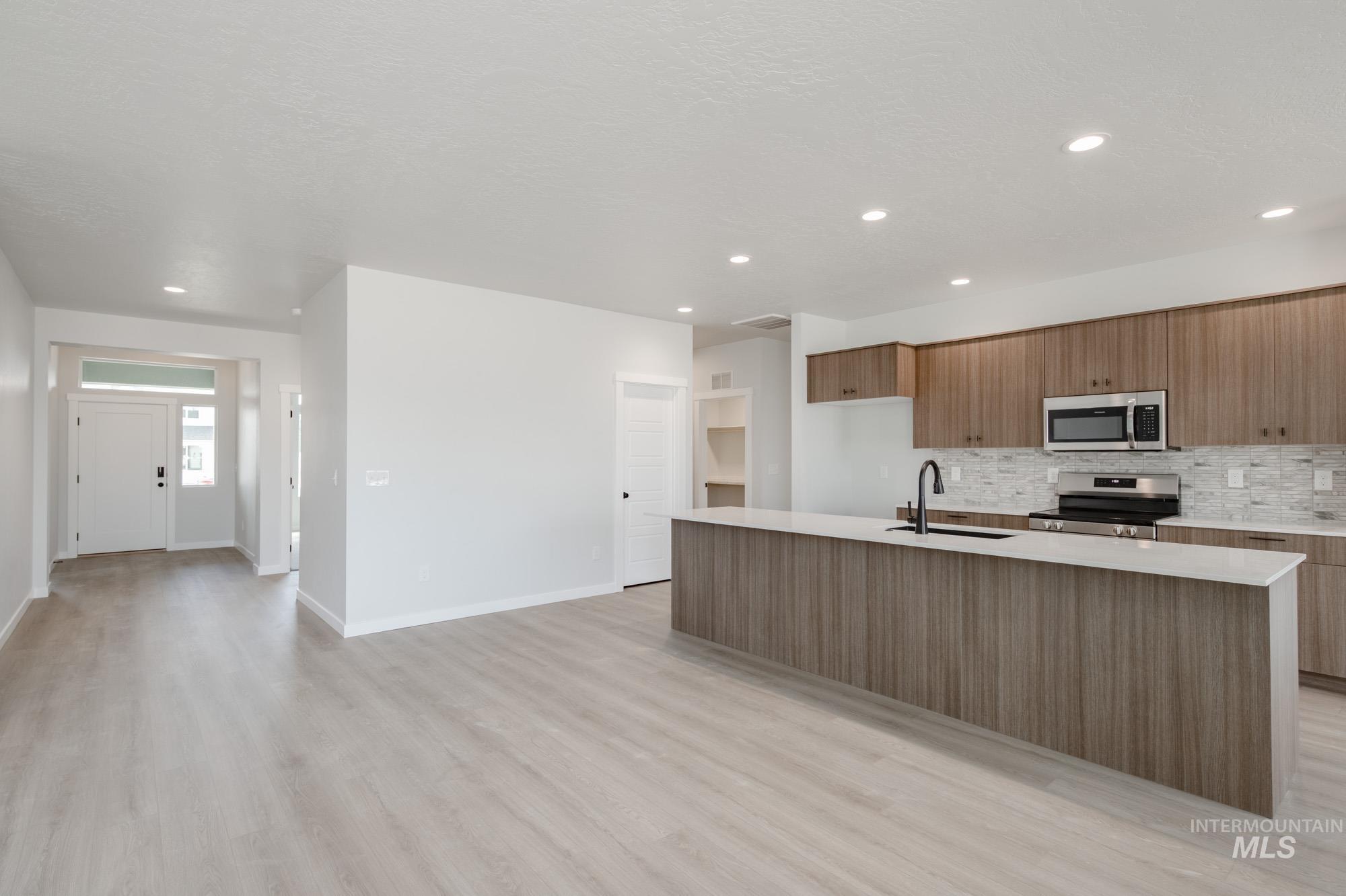 Kitchen featuring backsplash, brown cabinets, appliances with stainless steel finishes, a center island with sink, and recessed lighting