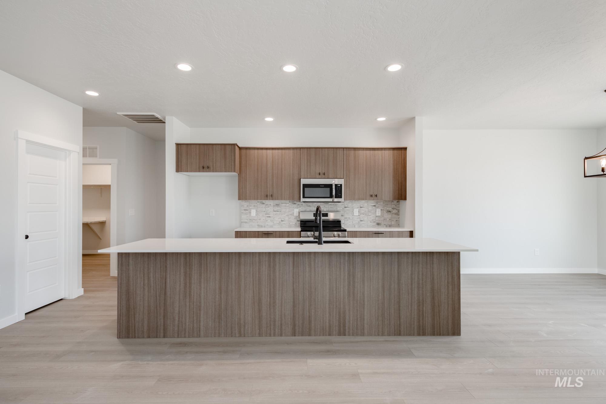 Kitchen featuring tasteful backsplash, brown cabinets, modern cabinets, light wood finished floors, and an island with sink