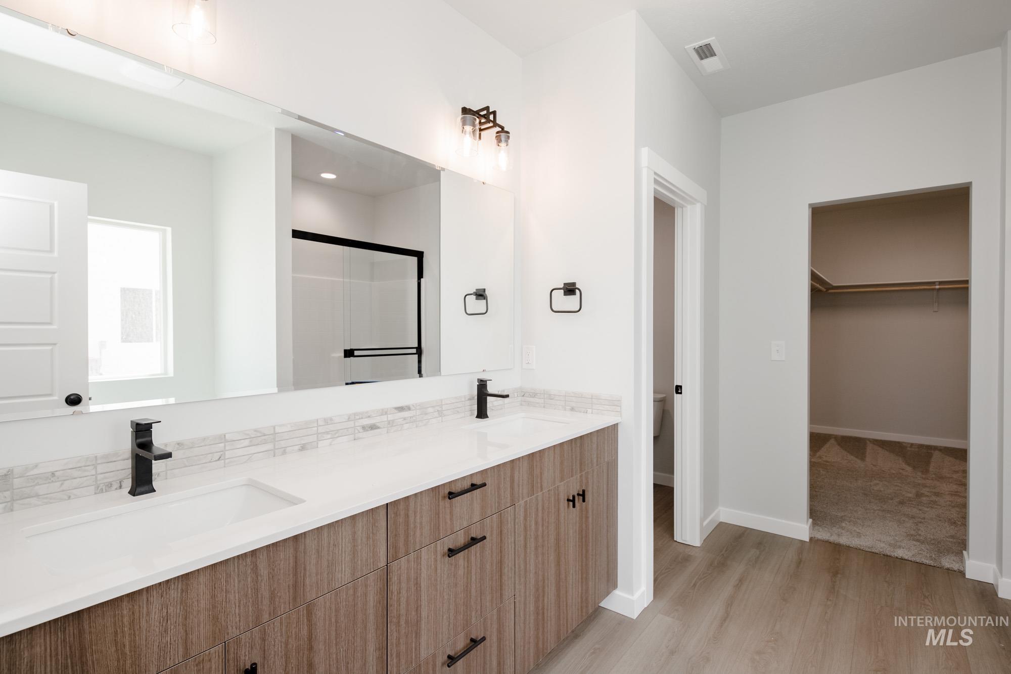 Bathroom with light wood-type flooring, a spacious closet, a stall shower, and double vanity