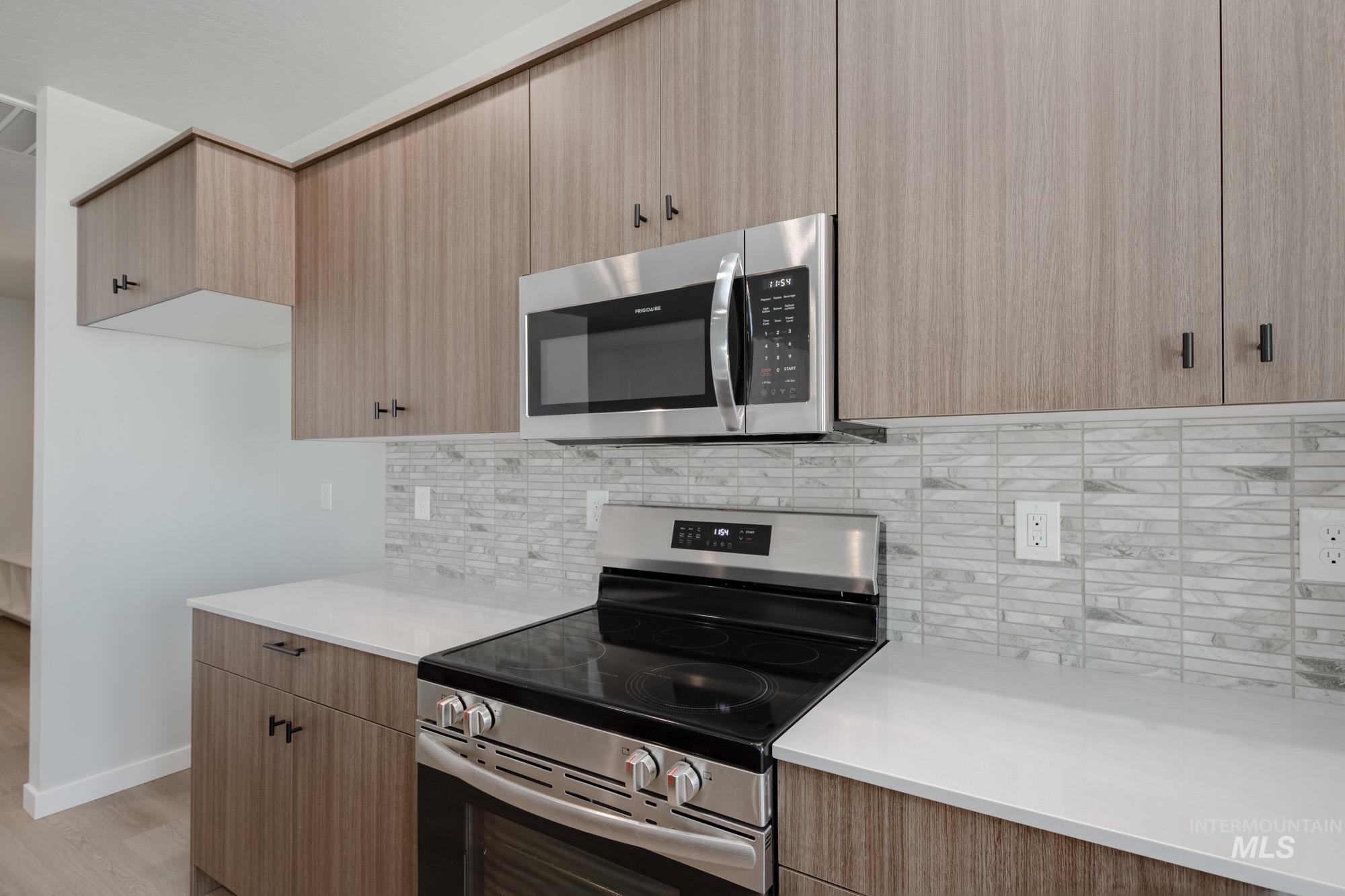 Kitchen with stainless steel appliances, decorative backsplash, modern cabinets, light stone counters, and light wood-style floors