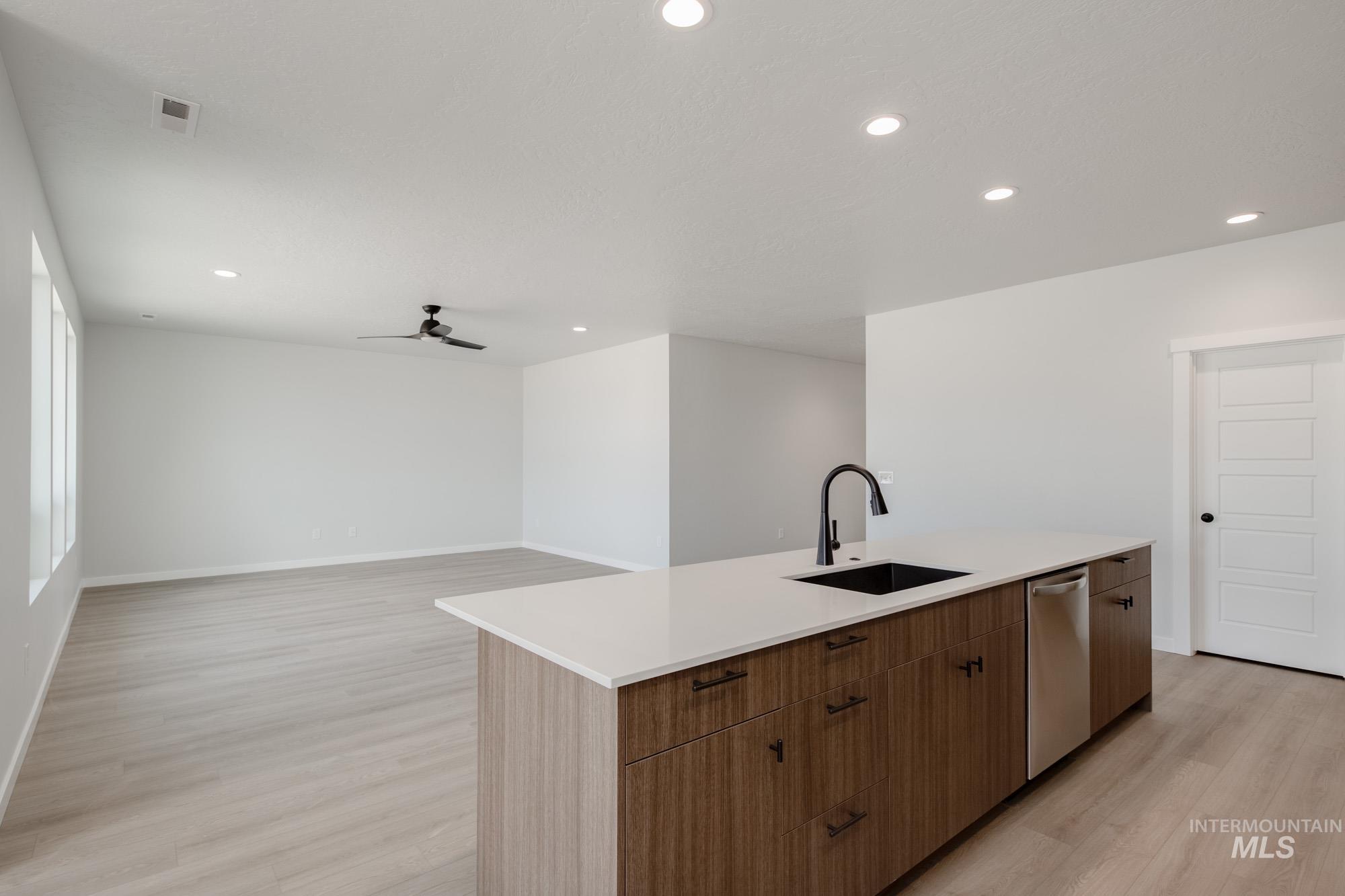 Kitchen with light wood-type flooring, recessed lighting, brown cabinetry, an island with sink, and modern cabinets