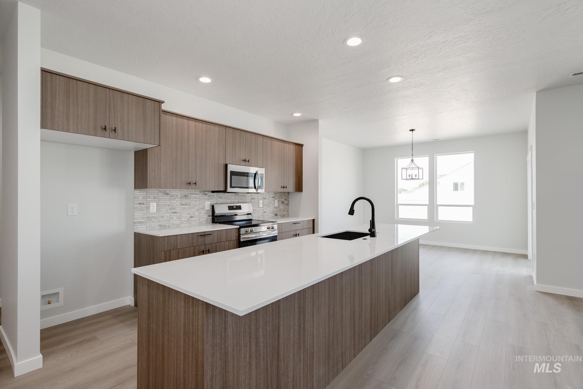 Kitchen featuring a kitchen island with sink, appliances with stainless steel finishes, backsplash, light stone countertops, and modern cabinets