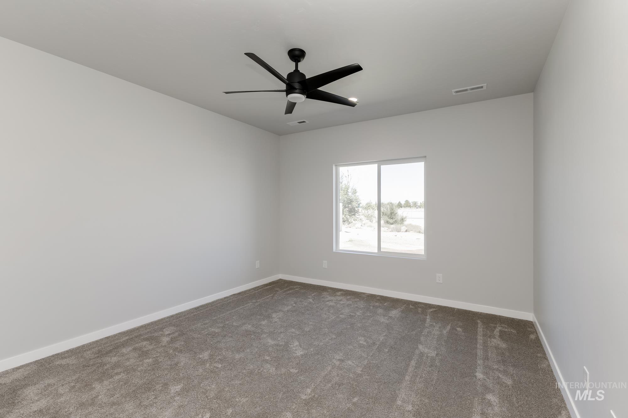 Empty room with dark colored carpet and a ceiling fan