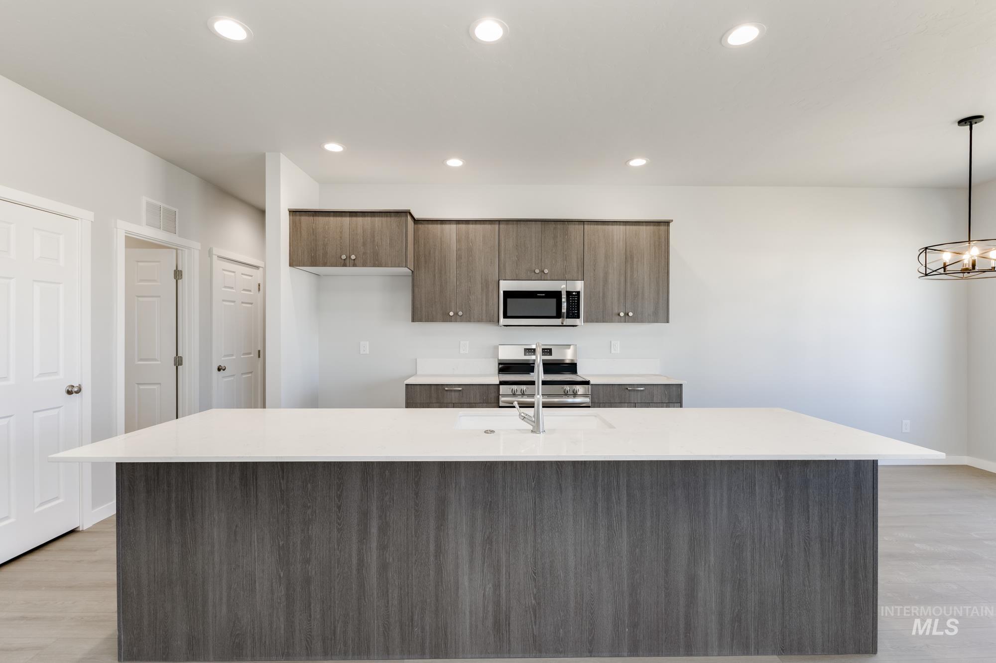 Kitchen with light wood-style floors, a kitchen island with sink, appliances with stainless steel finishes, light stone counters, and recessed lighting