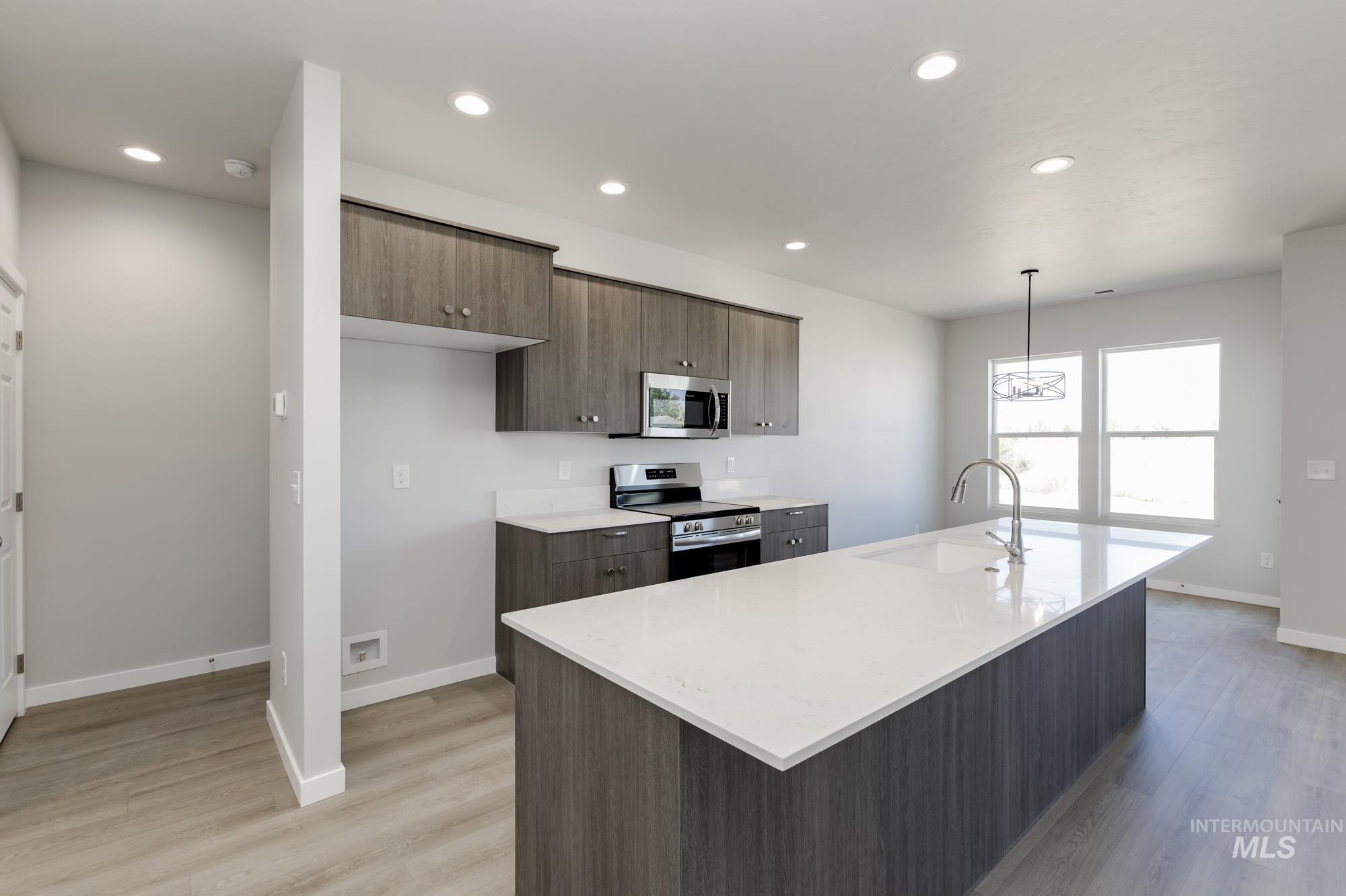 Kitchen featuring appliances with stainless steel finishes, a center island with sink, recessed lighting, pendant lighting, and light wood finished floors