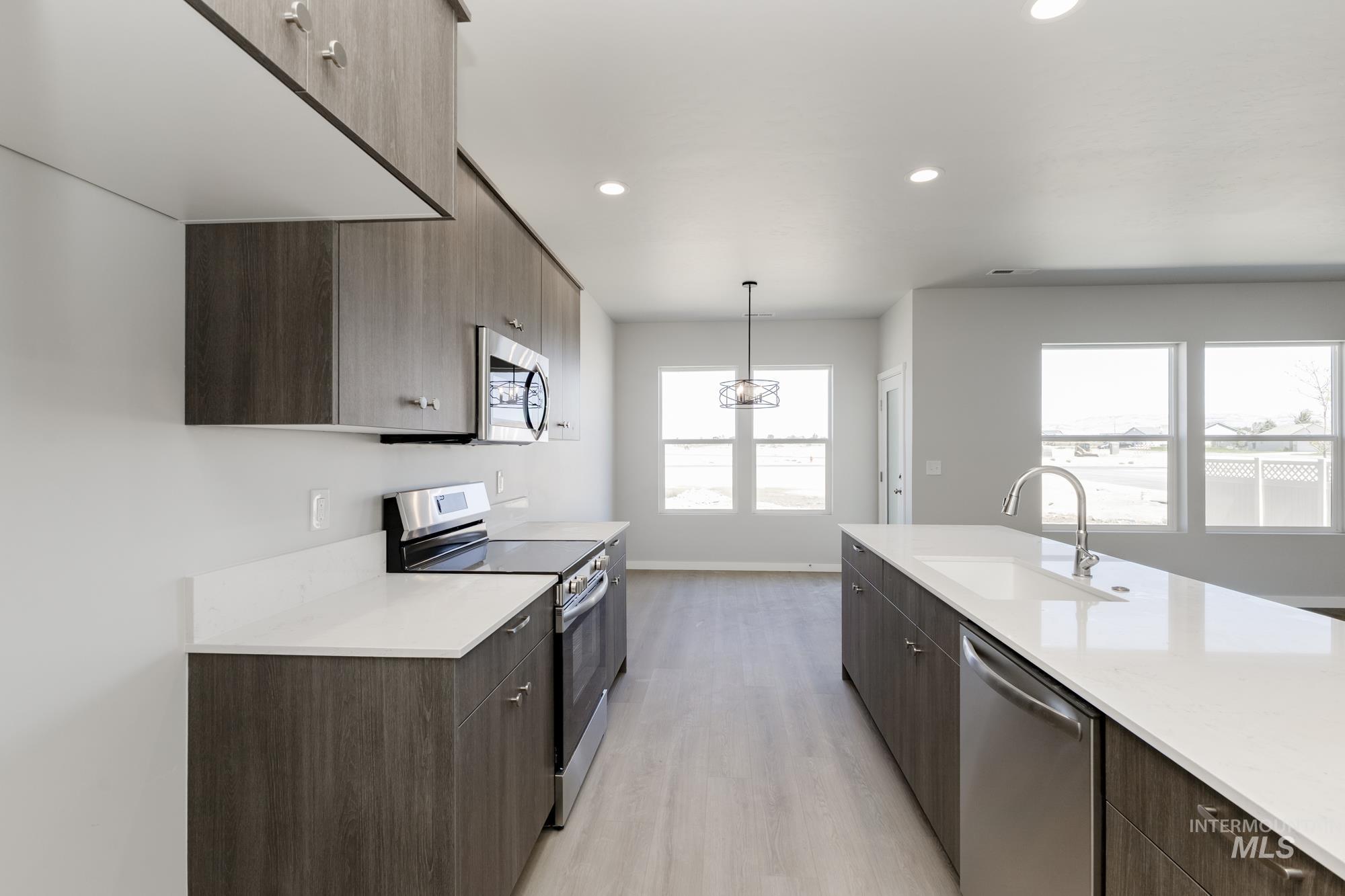 Kitchen with modern cabinets, appliances with stainless steel finishes, dark brown cabinetry, light wood-style floors, and decorative light fixtures