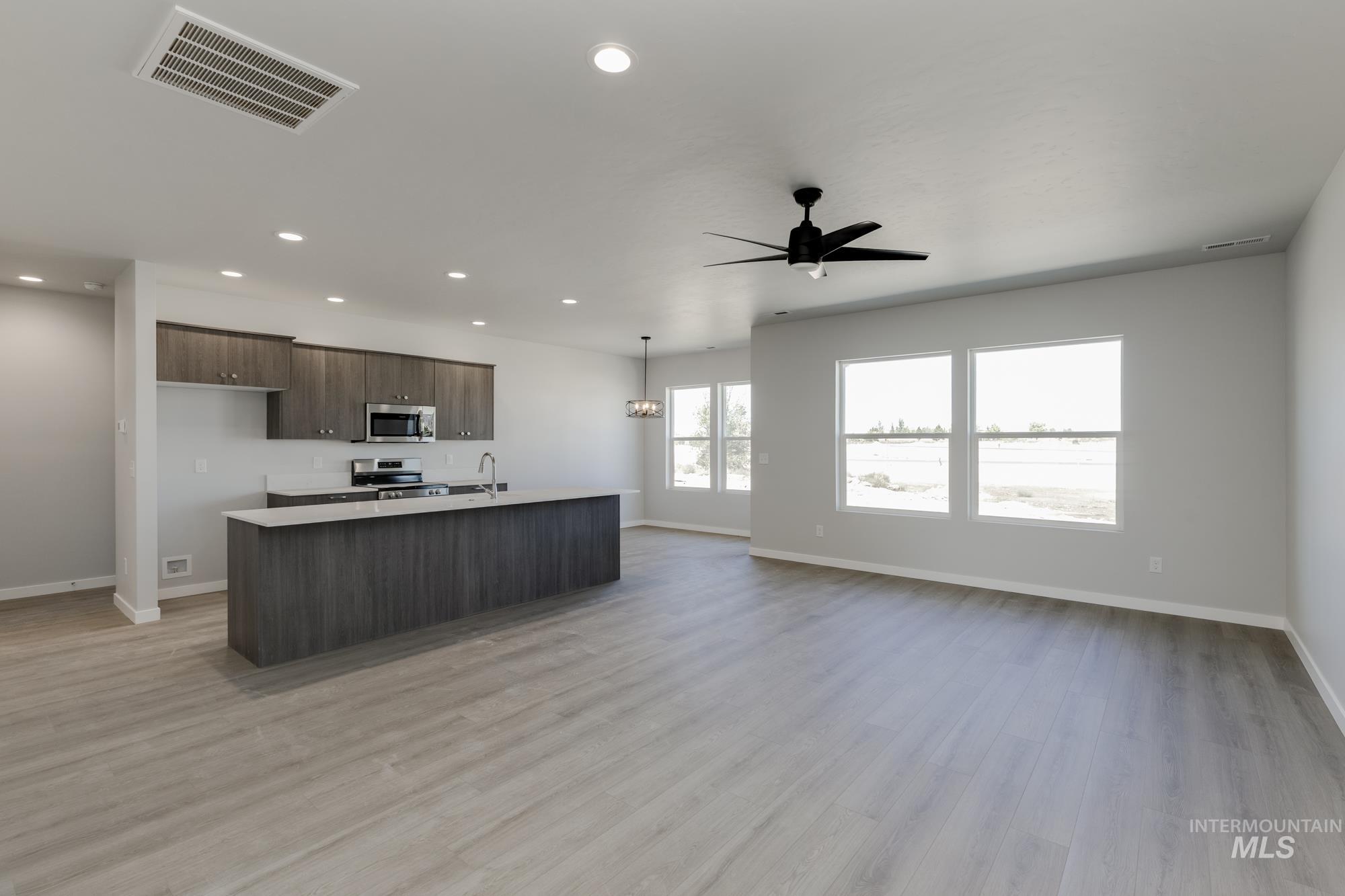 Kitchen featuring dark brown cabinets, an island with sink, light countertops, open floor plan, and light wood-style floors