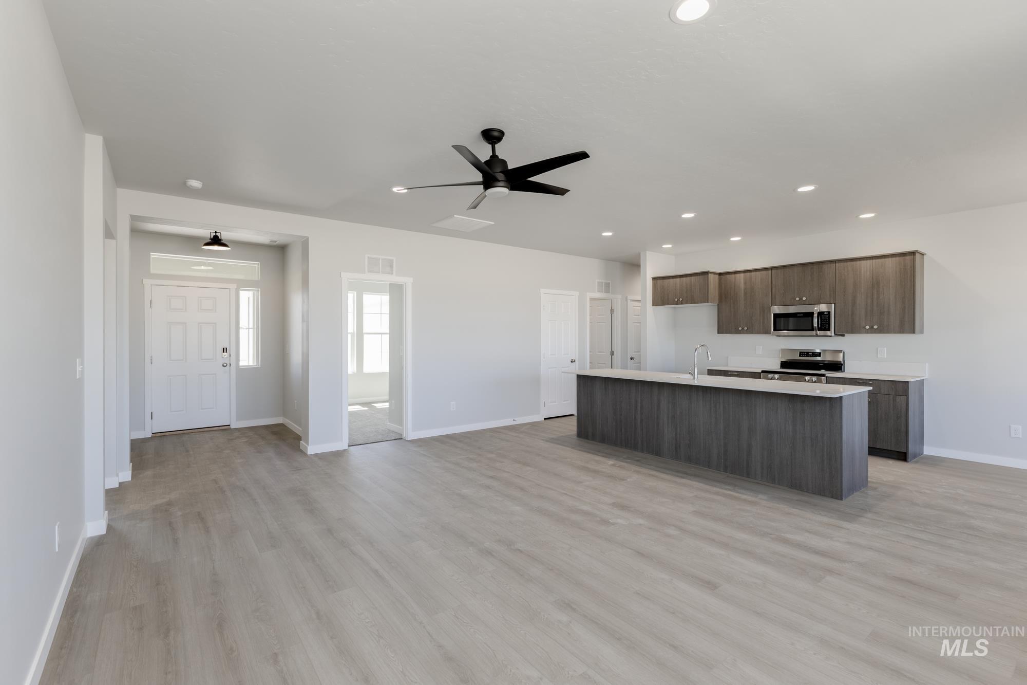 Kitchen with an island with sink, light countertops, open floor plan, light wood-style floors, and ceiling fan