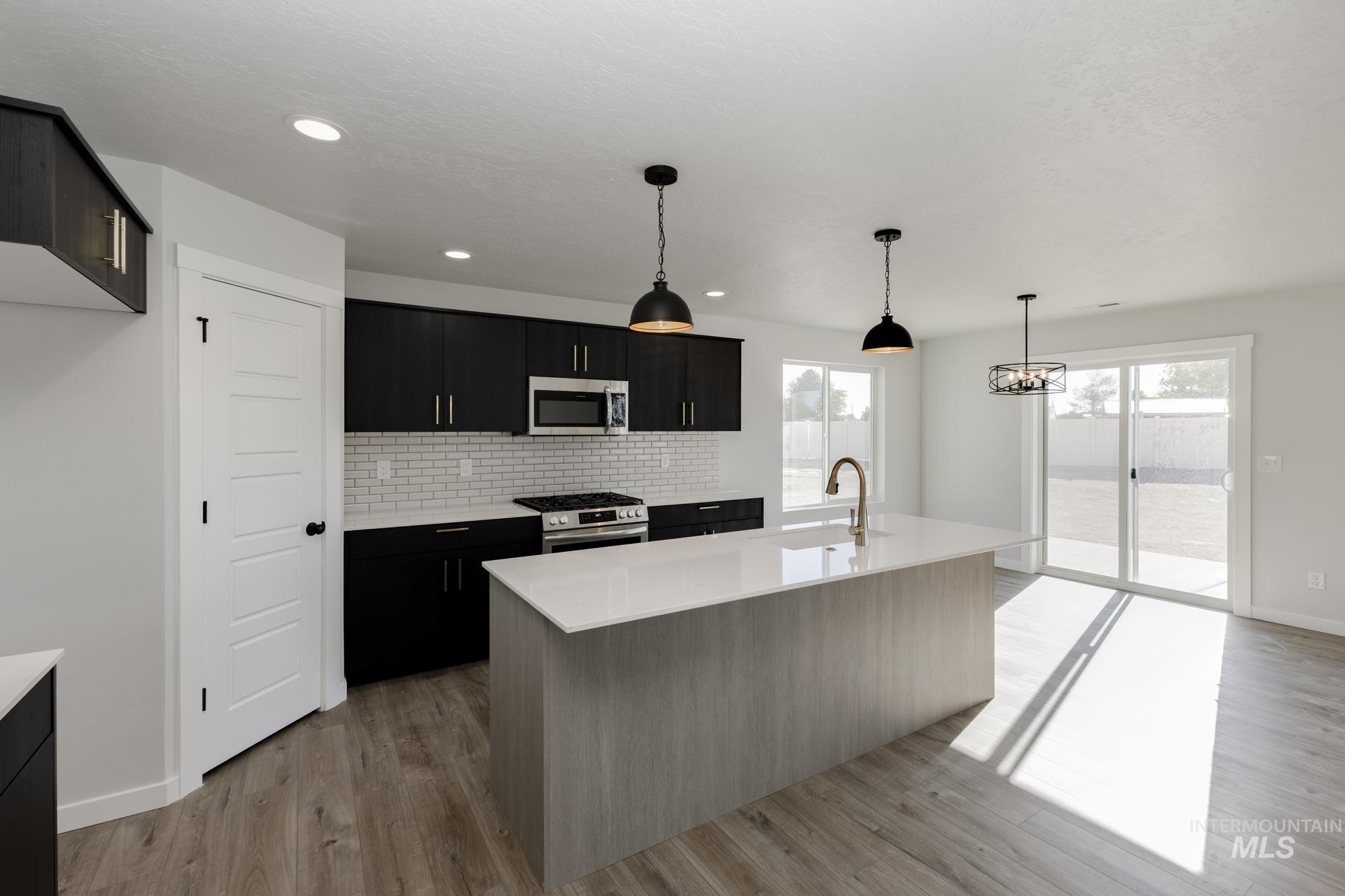 Kitchen featuring backsplash, a kitchen island with sink, hanging light fixtures, appliances with stainless steel finishes, and light wood-type flooring